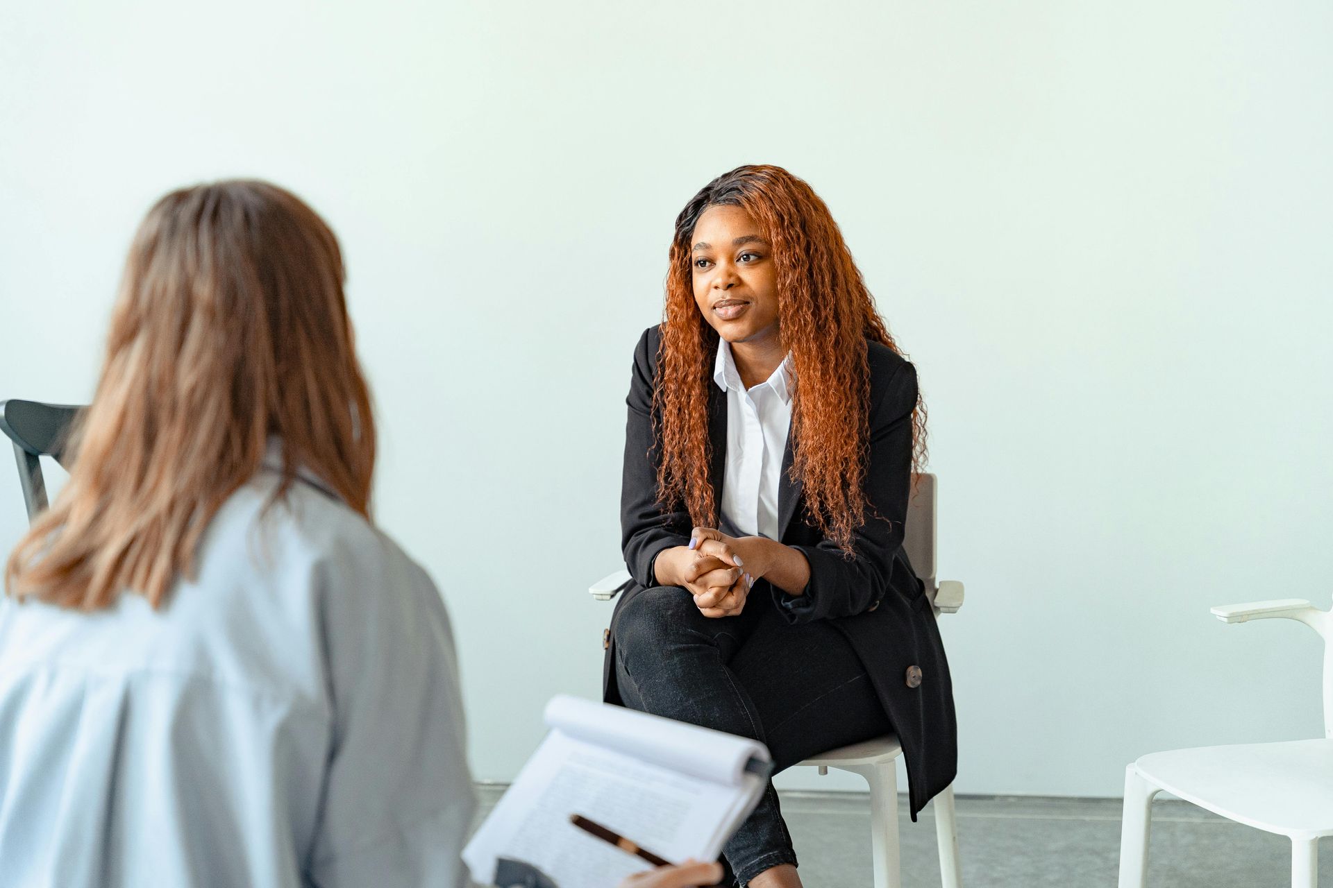 A woman is sitting in a chair talking to another woman.