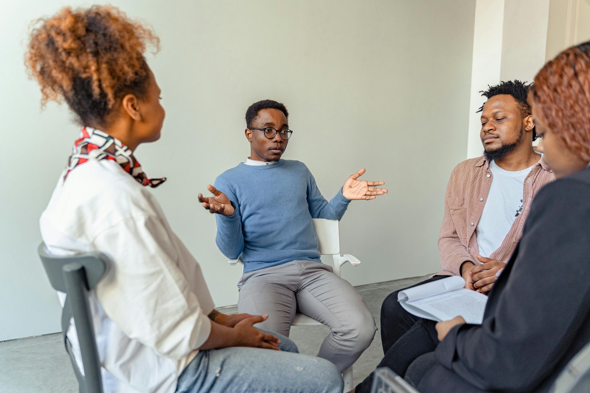 Four people in a small meeting room discussing, with one person gesturing while others listen