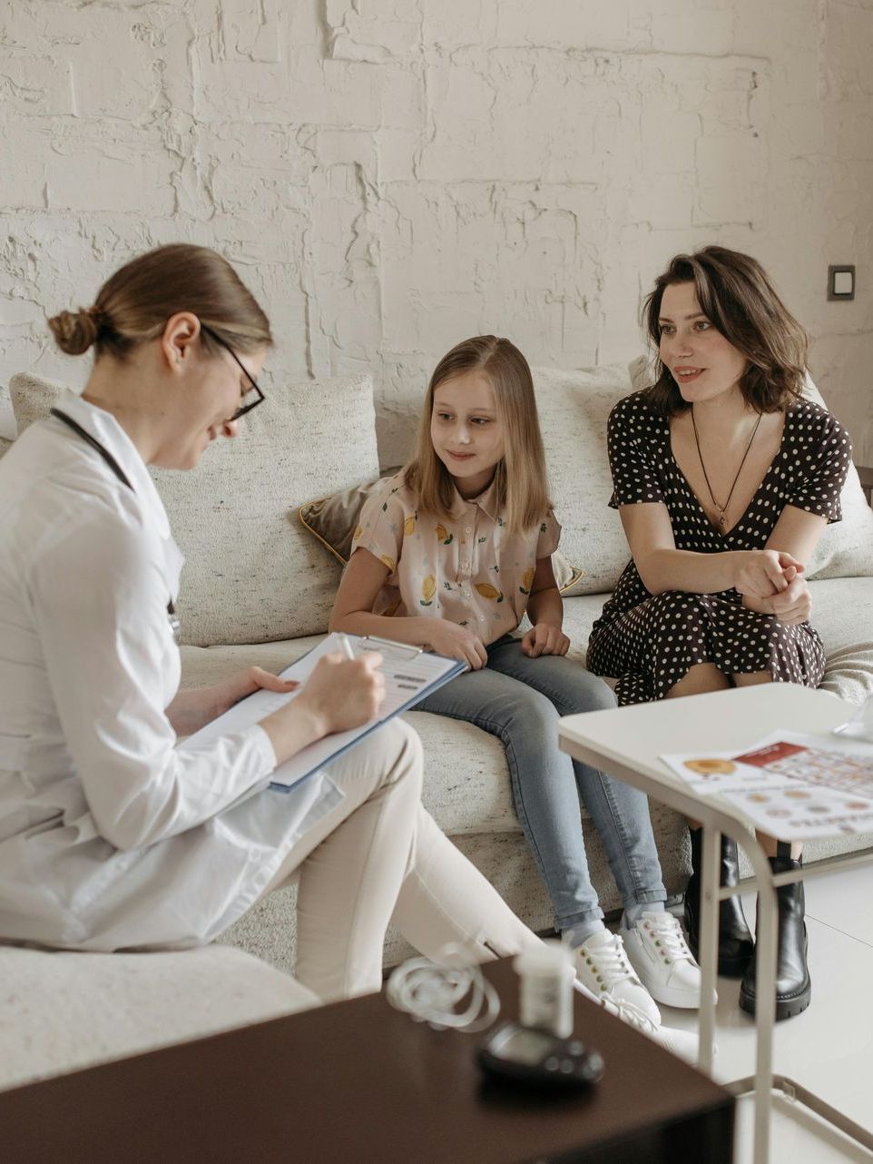 A doctor is sitting on a couch talking to a woman and a little girl.
