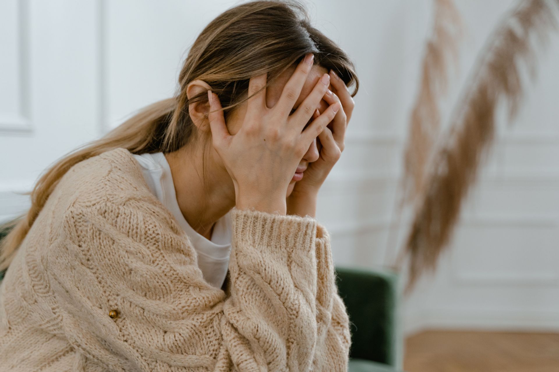 Distressed person with hands covering face in a beige sweater, seated indoors