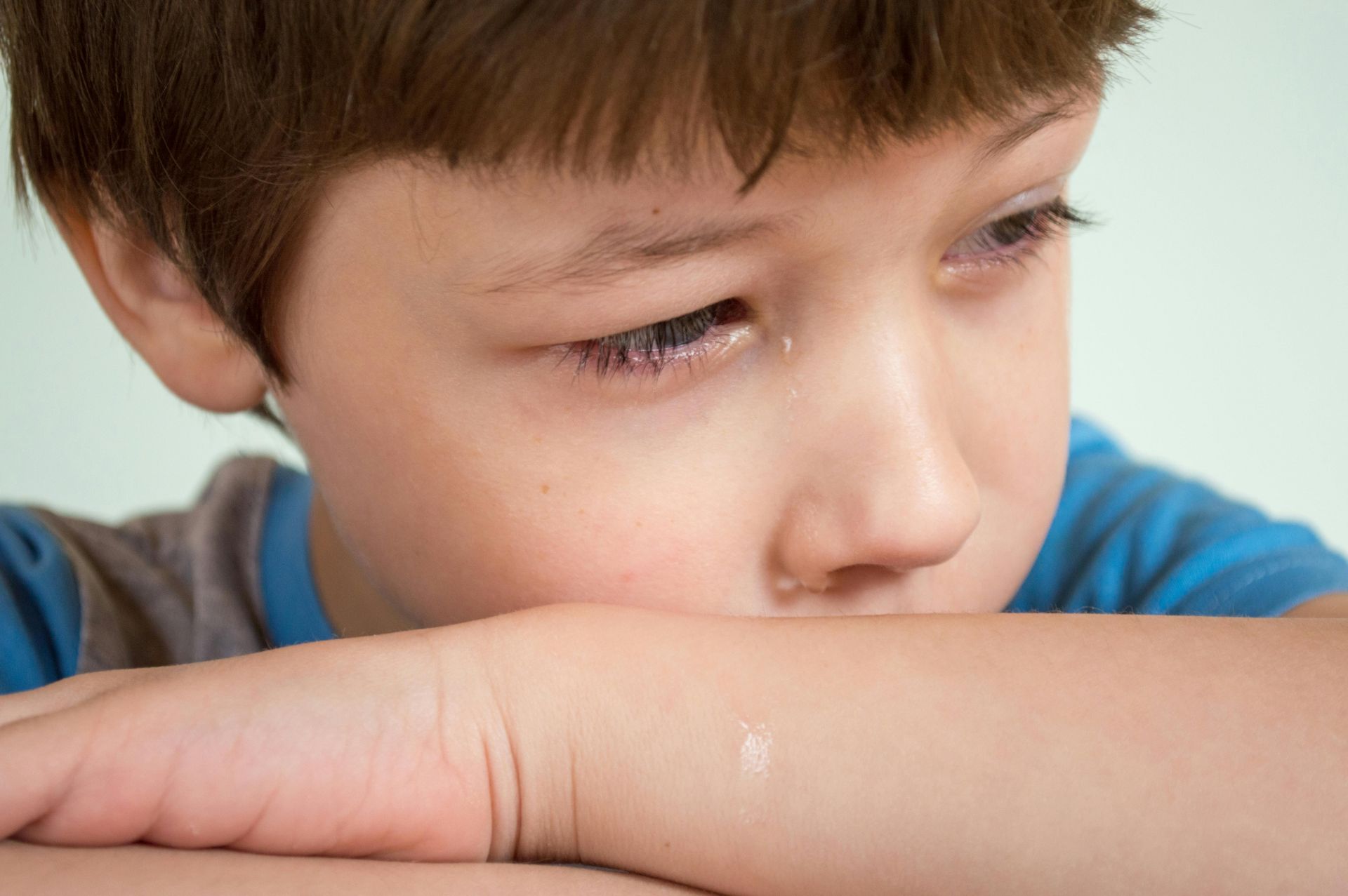 A young boy is sitting with his head resting on his arm.