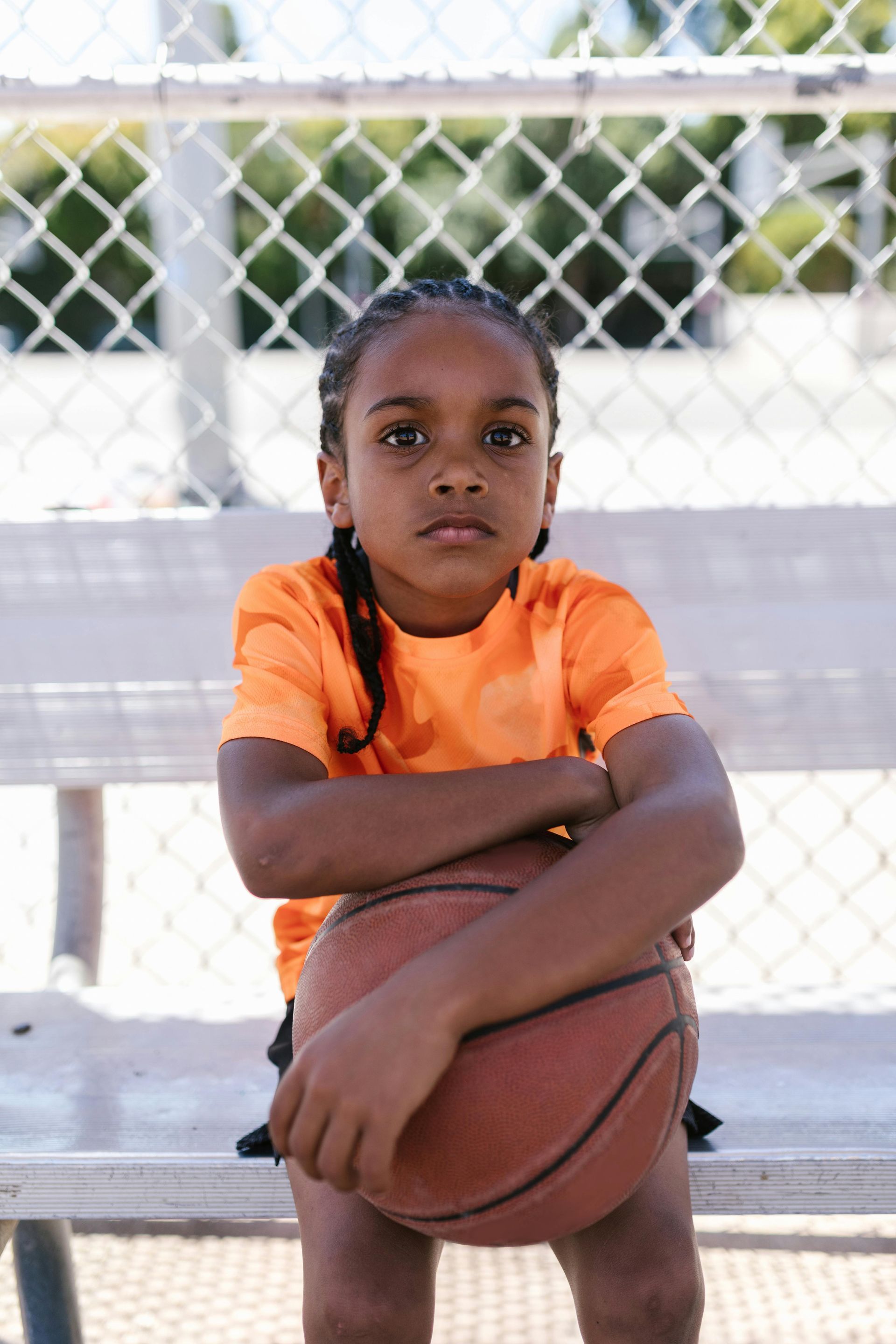 A young boy is sitting on a bench holding a basketball.