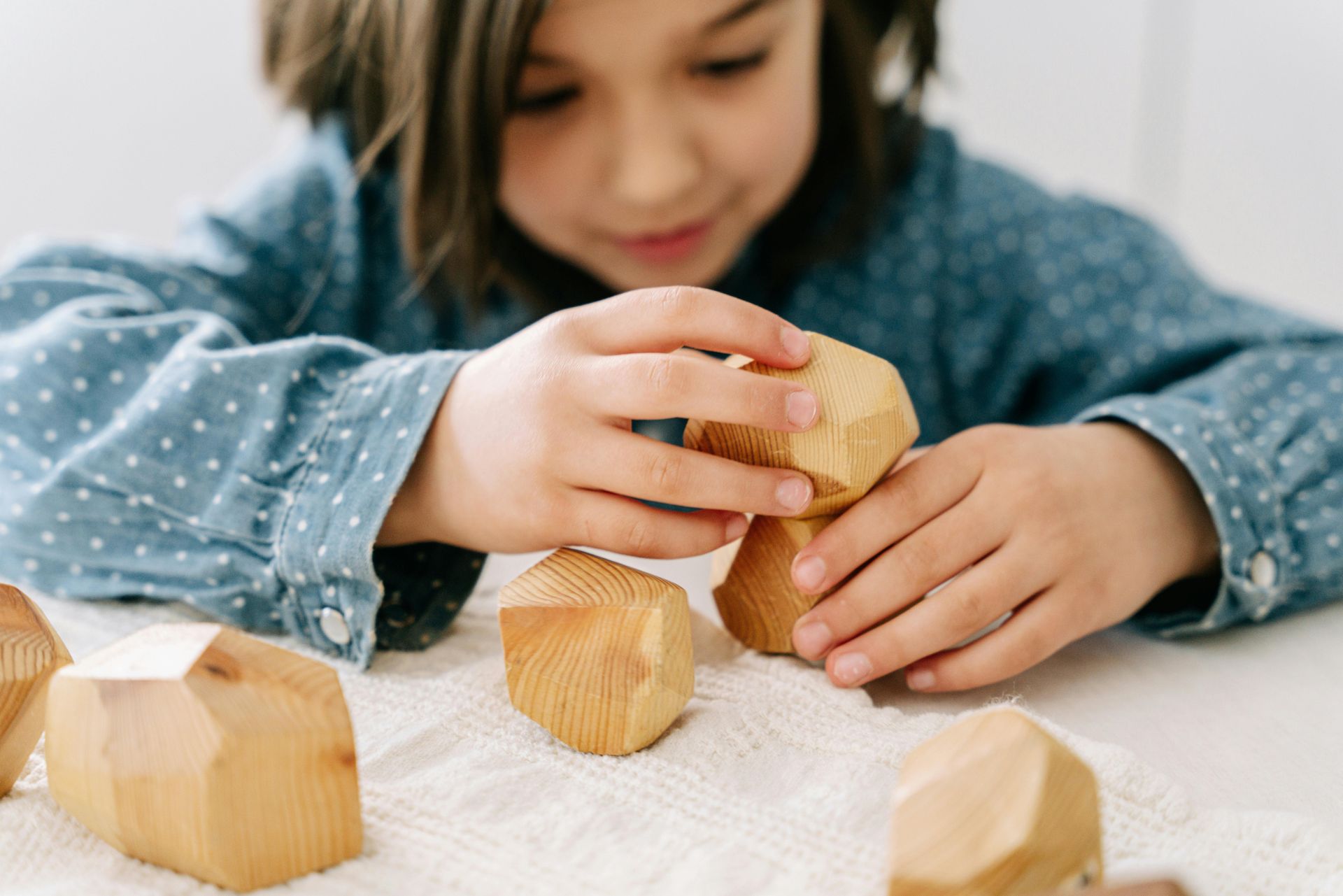 A little girl is playing with wooden blocks on a table.