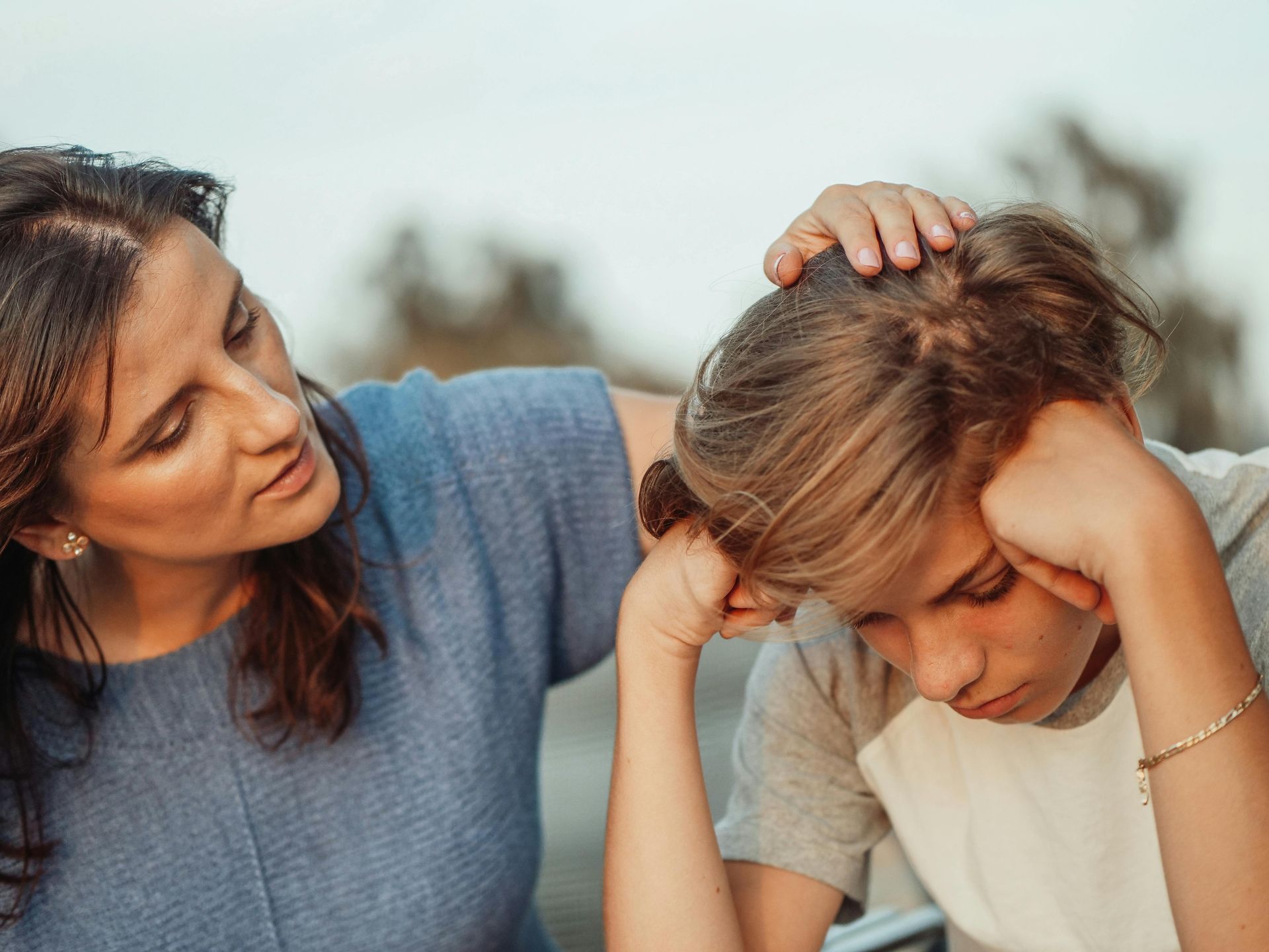 A woman is comforting a young boy who is sitting down with his head in his hands.