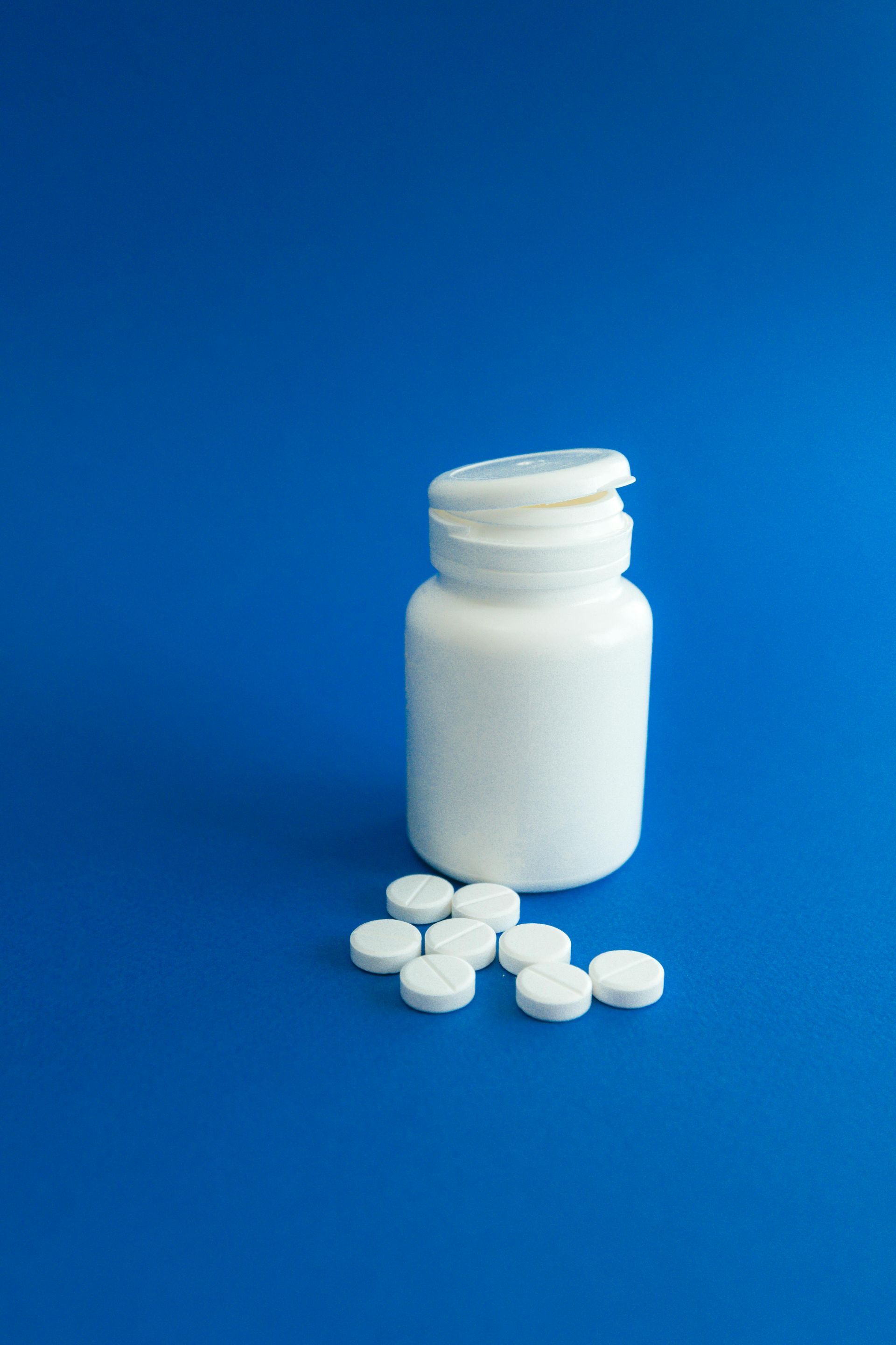 White pill bottle with several white pills on a blue surface.