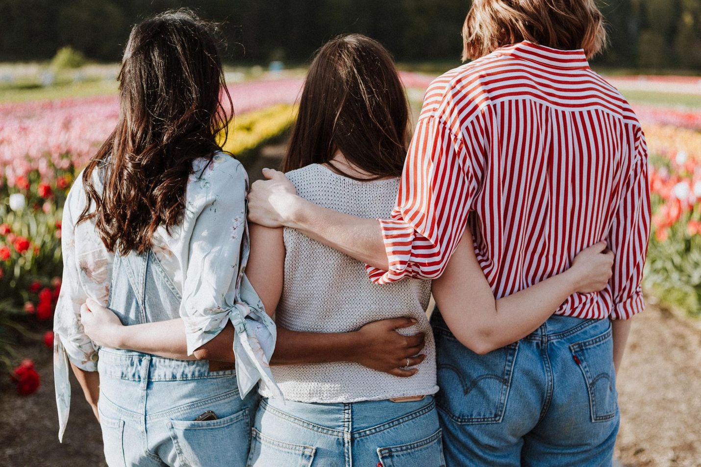 Three women are hugging each other in a field of flowers.