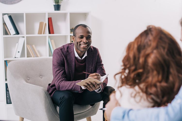 A man is sitting in a chair talking to a woman.