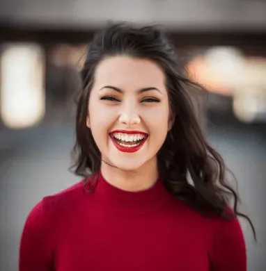 A woman in a red sweater is laughing and wearing red lipstick.