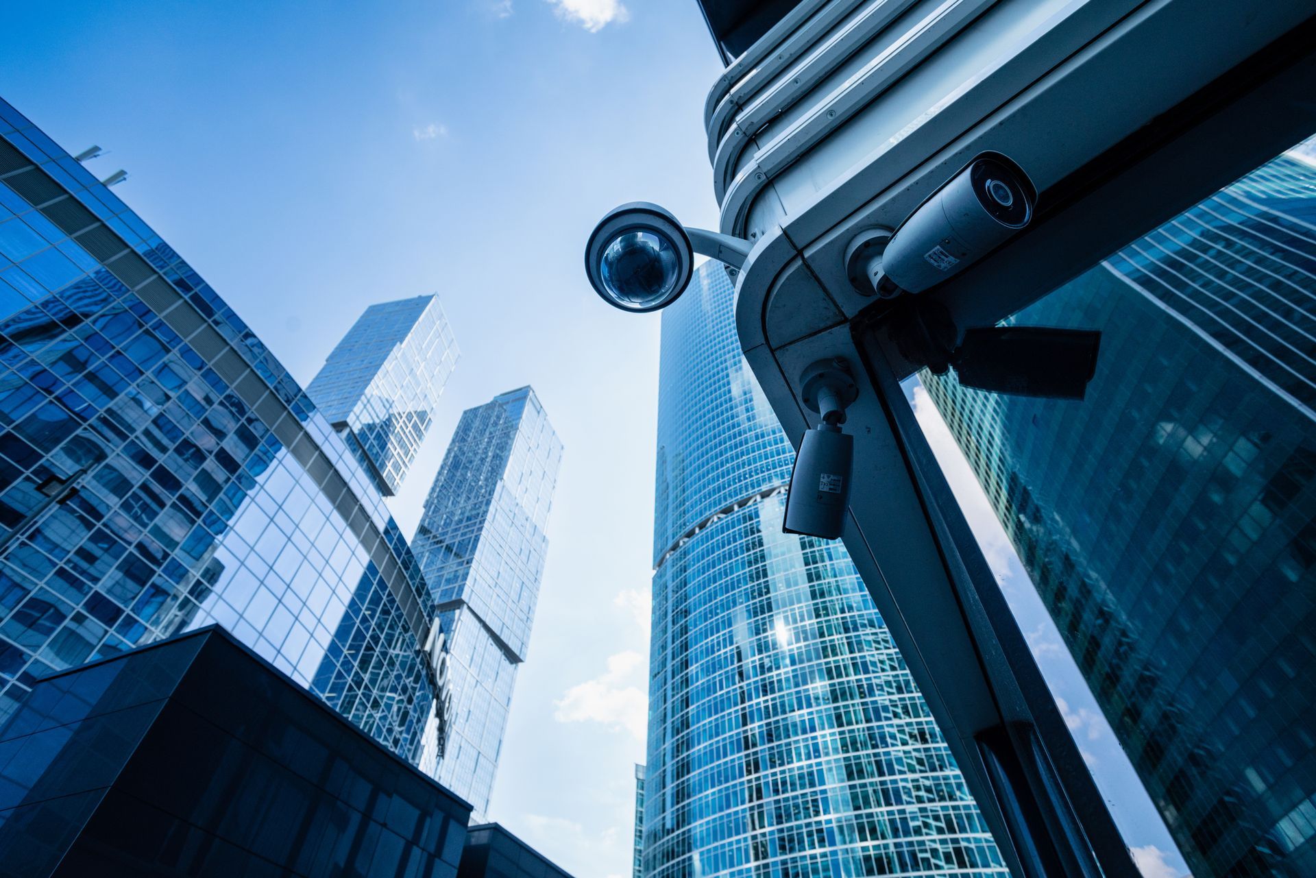 A security camera is mounted on the side of a building in a city.