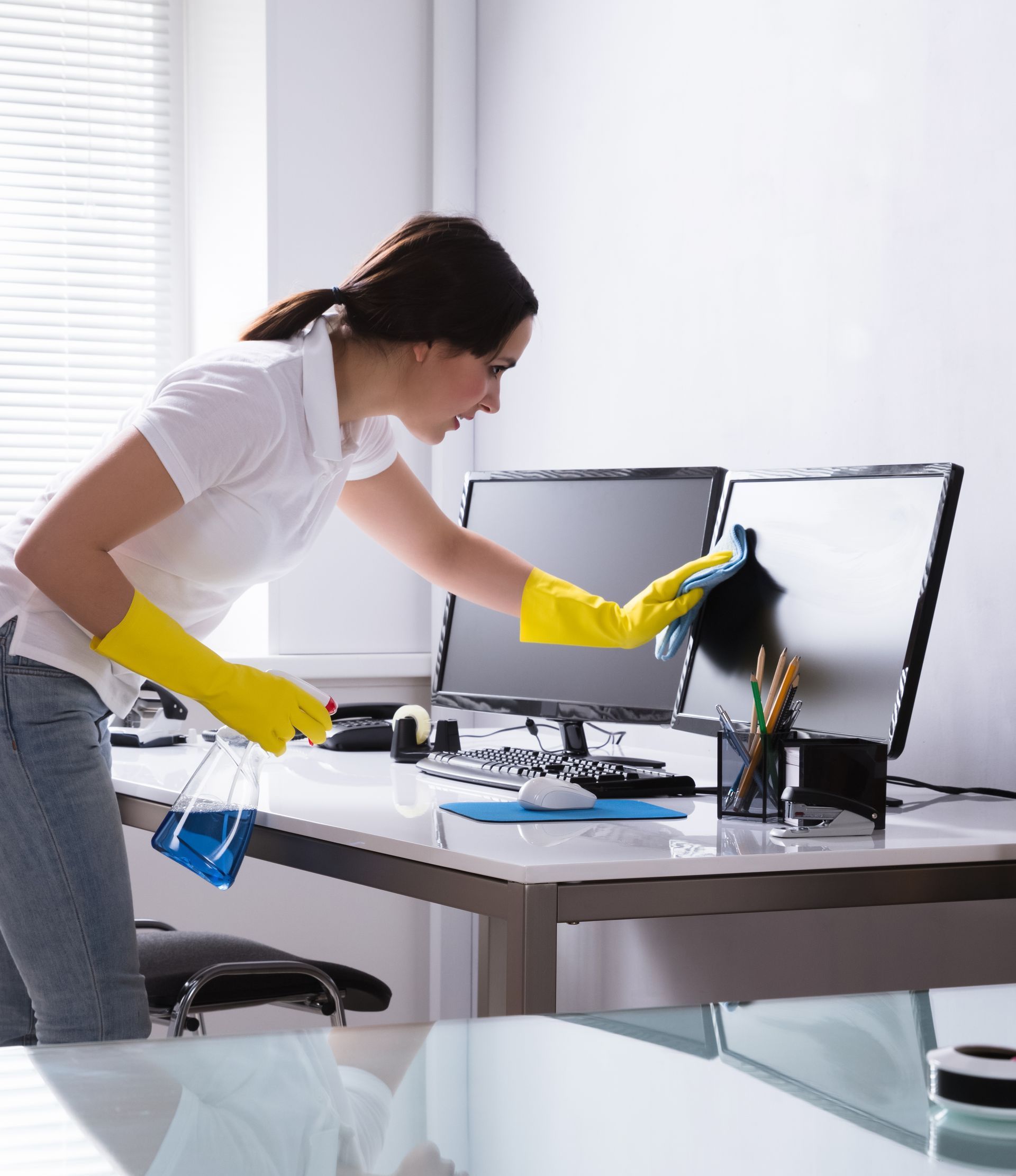 Bucket full of house clenaing stuff on a kitchen desk with a female holding it in rubber gloves.