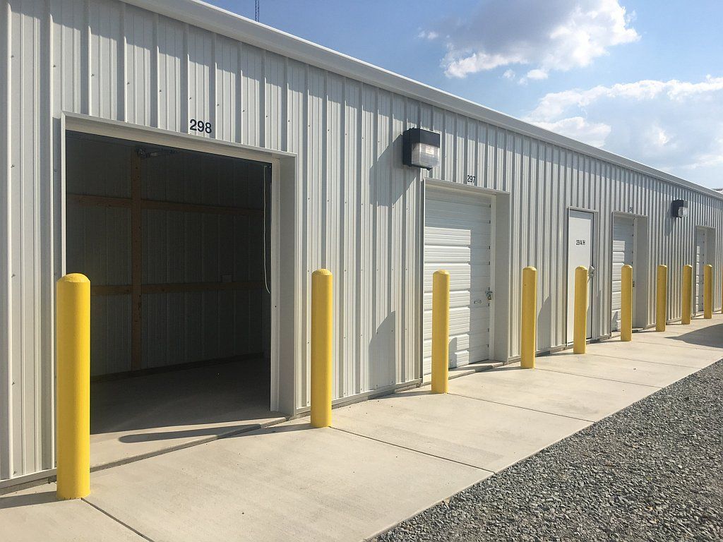 Exterior view of a storage facility with open unit, yellow bollards, and gray concrete walkway.