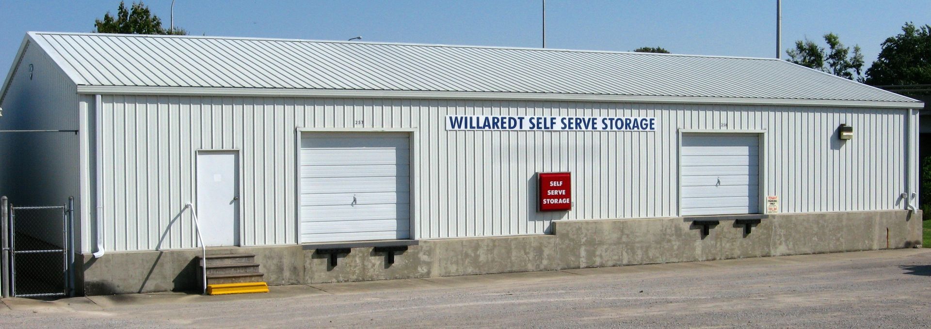 A white metal building with a corrugated roof, two garage doors, and a red fire box.