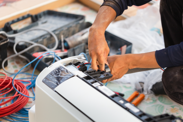 Hands repairing a white printer with tools and tangled cables on a workbench