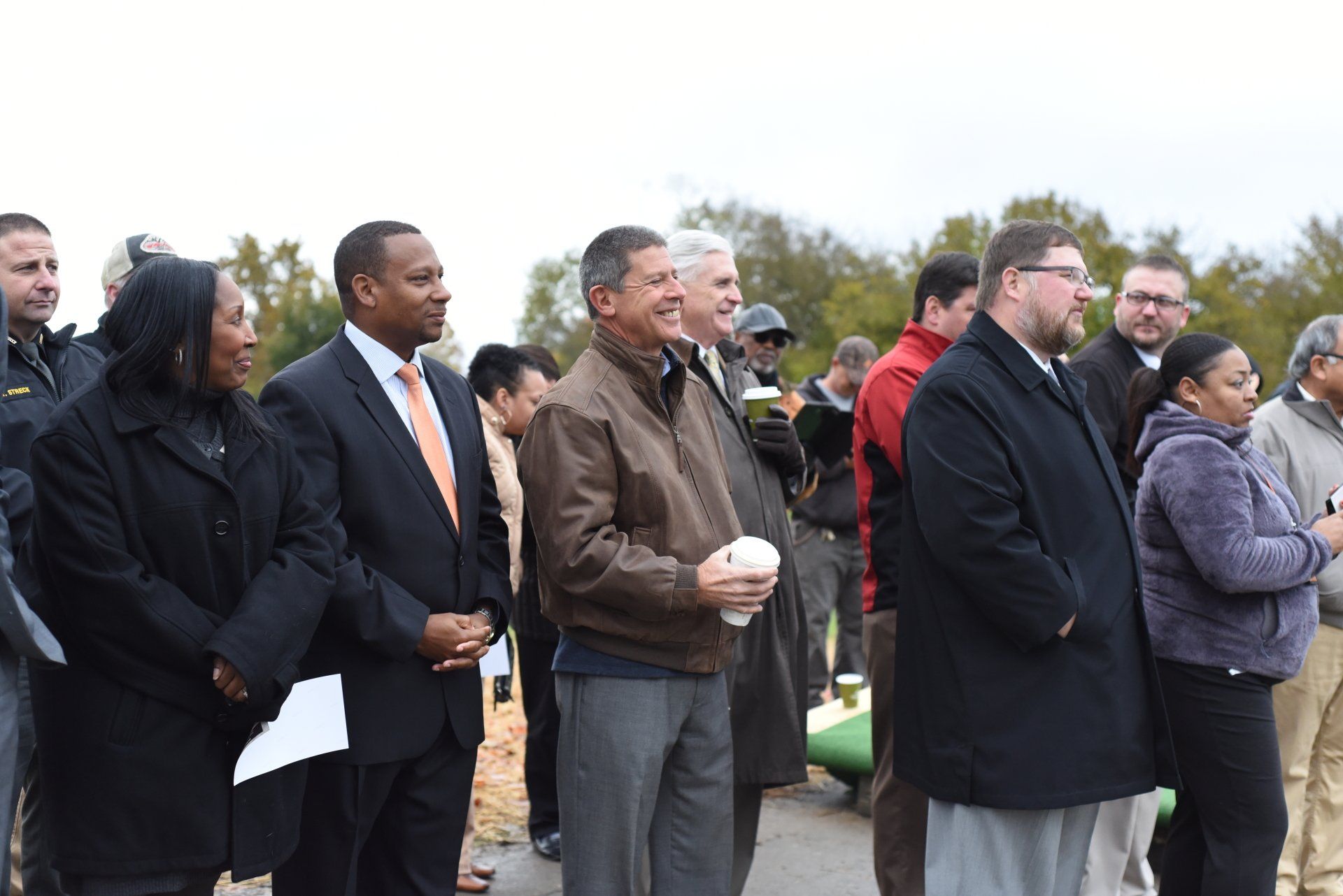 Group of diverse people standing outdoors, looking forward, some holding papers.