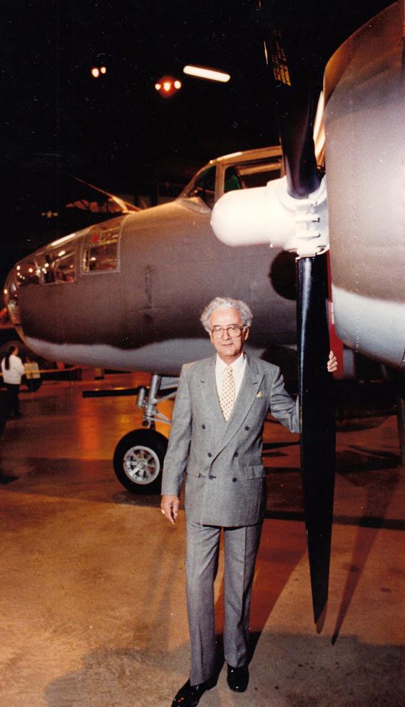 Man in a suit standing next to an airplane propeller in a hangar.