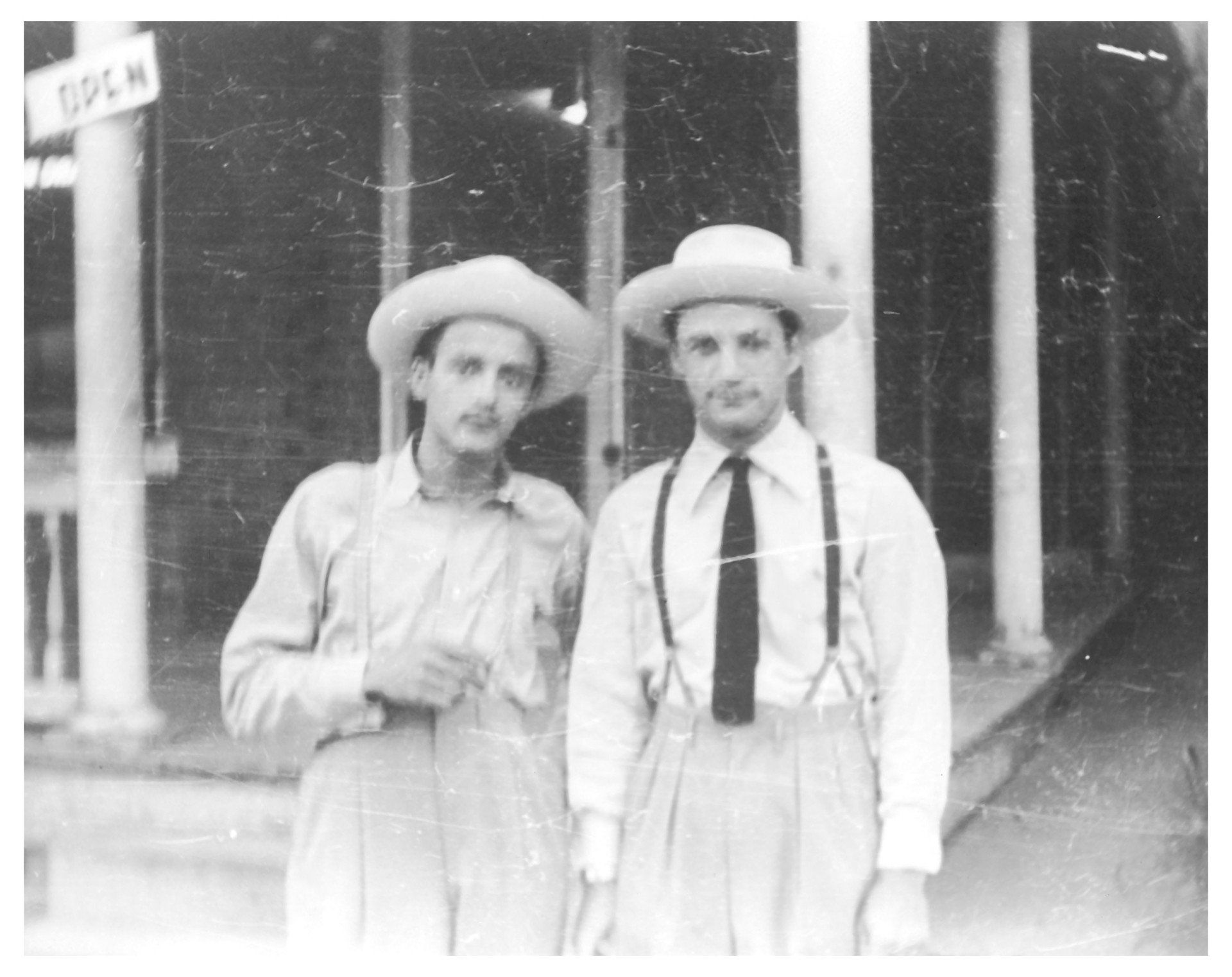Two men in straw hats and suspenders stand outside a building.