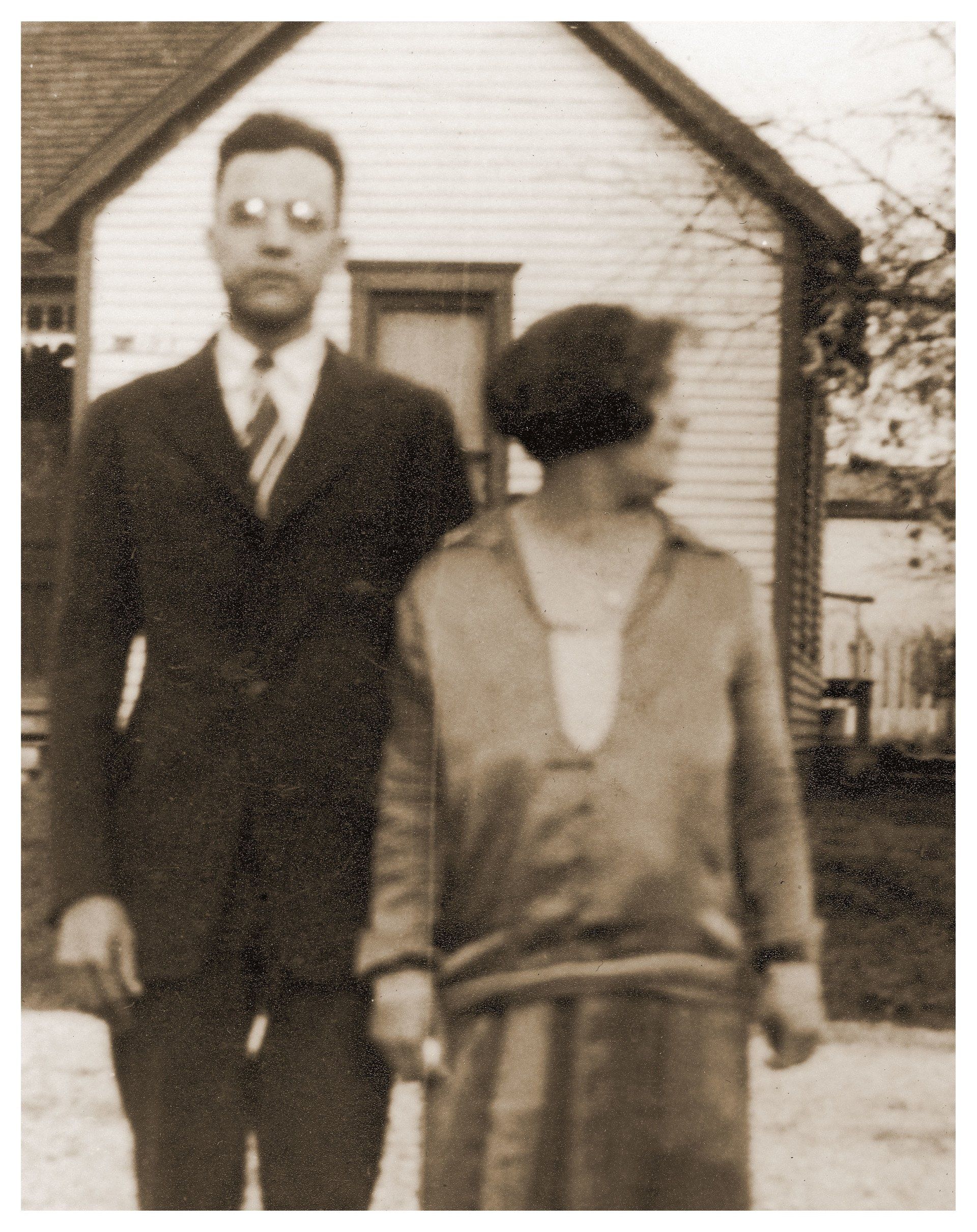 Man in suit and woman in dress stand in front of a house. Black and white photo.