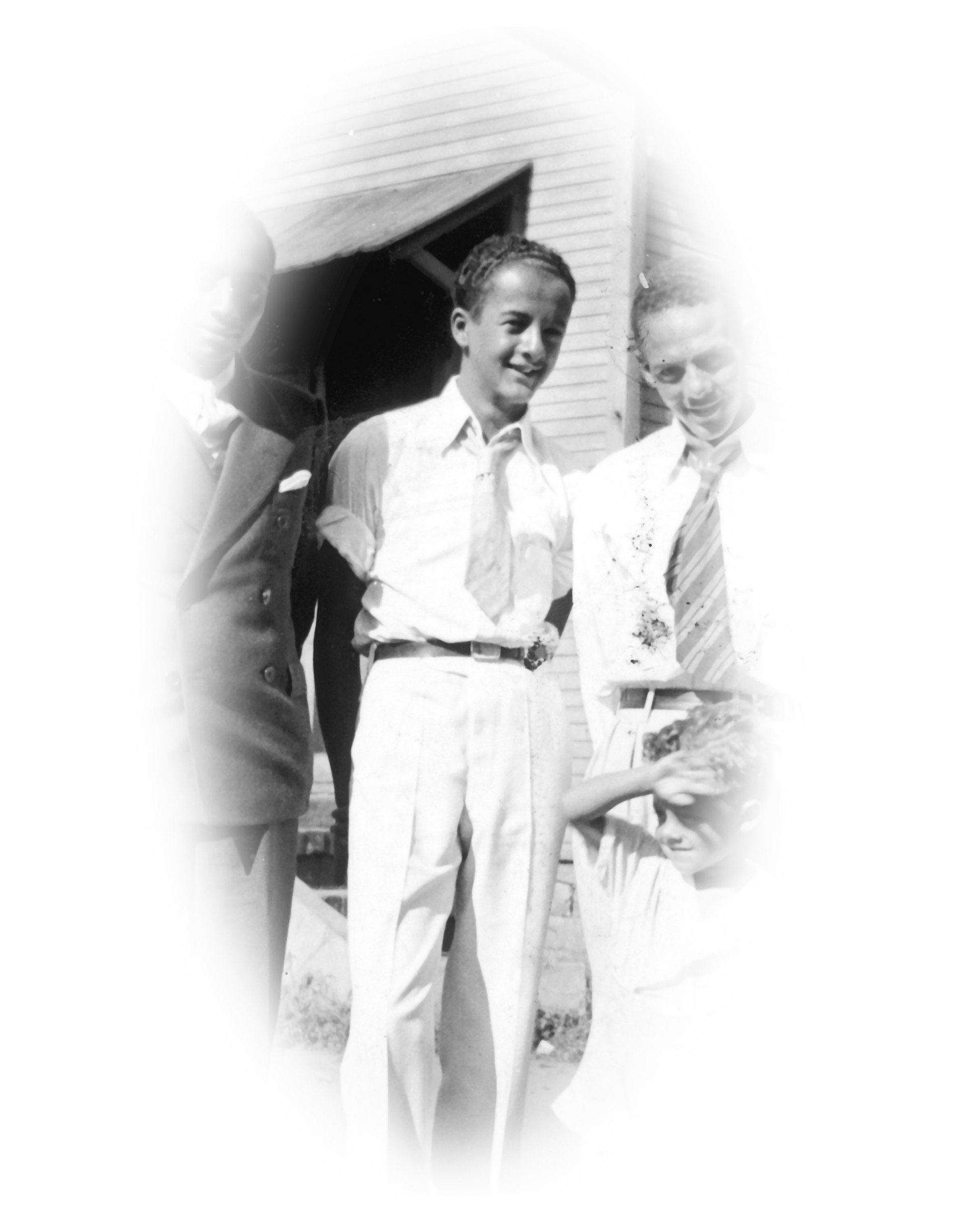 Three young men in light-colored clothing outdoors, smiling. One is center, holding a tie. Black and white photograph.