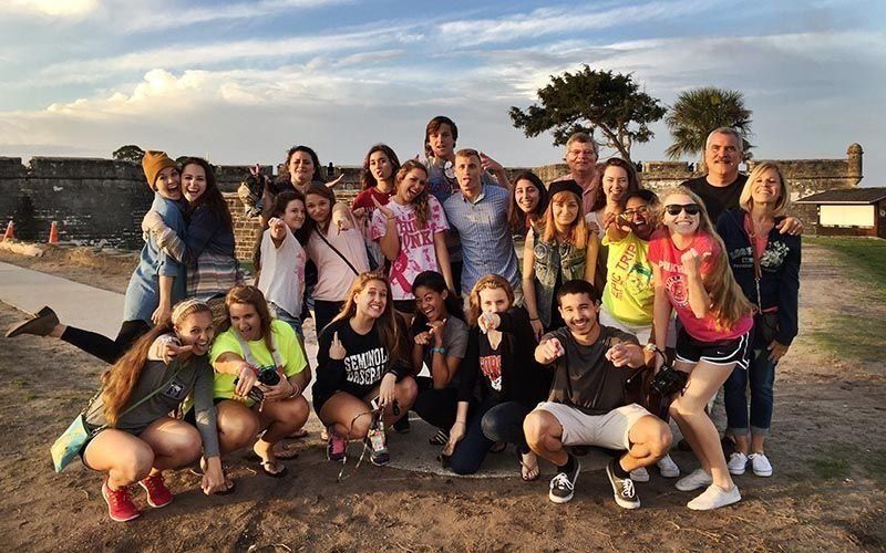 Group of young people posing at a historic fort, smiling at the camera, during the day.