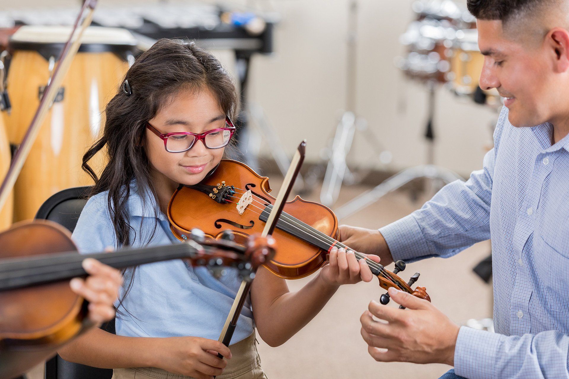 Girl in glasses learning violin with a teacher in a music room.