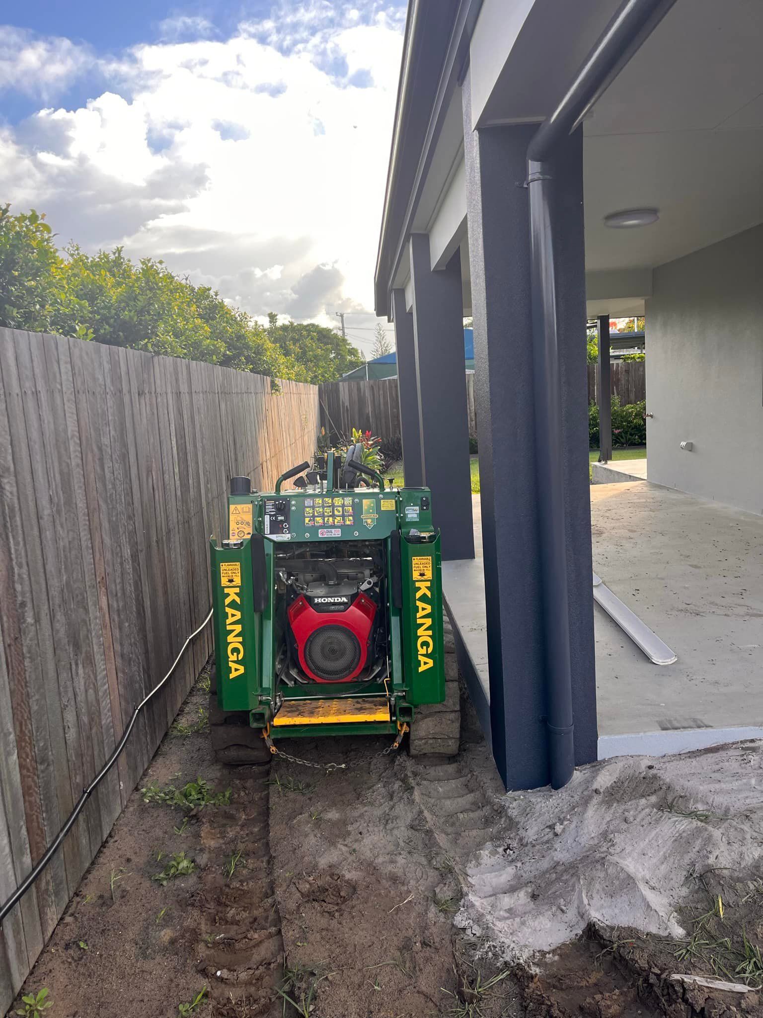Green Trencher Digging Along a Wooden Fence Next to a House — All Access Mini Earthworks  in Innes Park, QLD