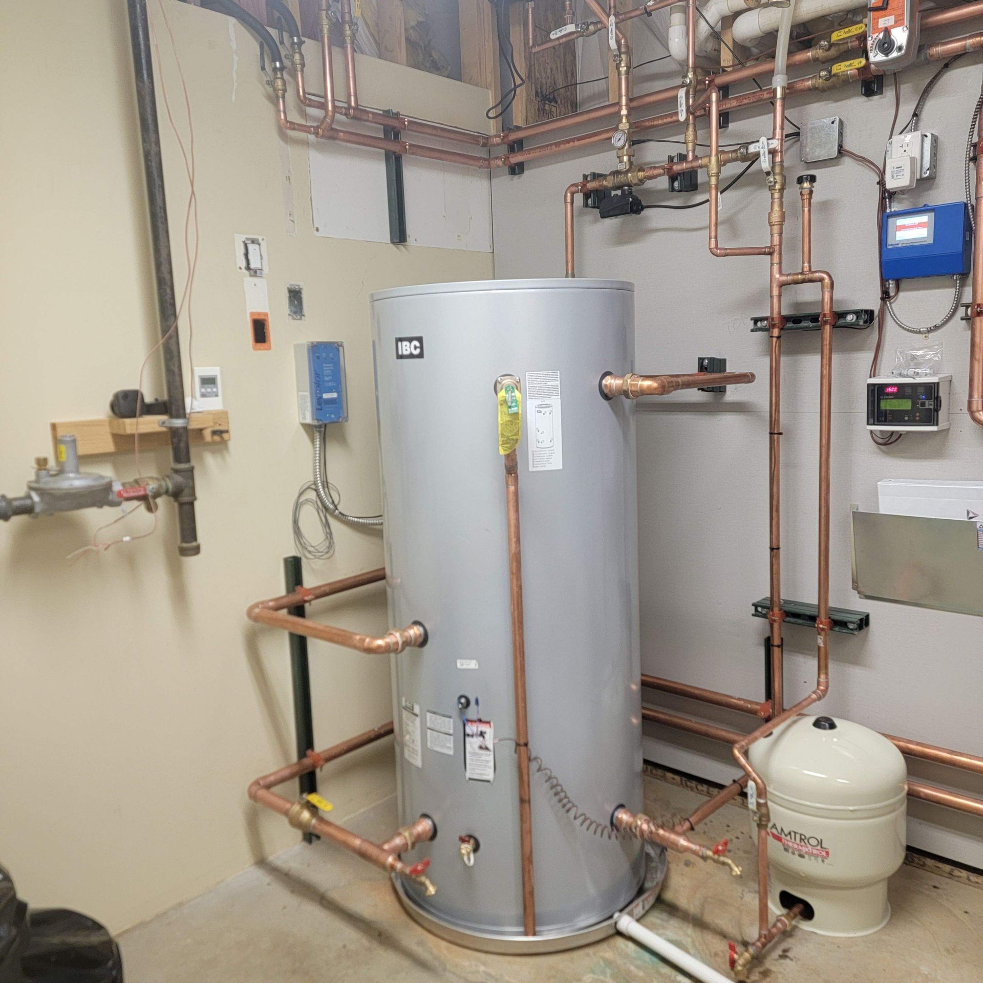 Plumbing room with a large silver water heater and copper piping on the walls and ceiling.