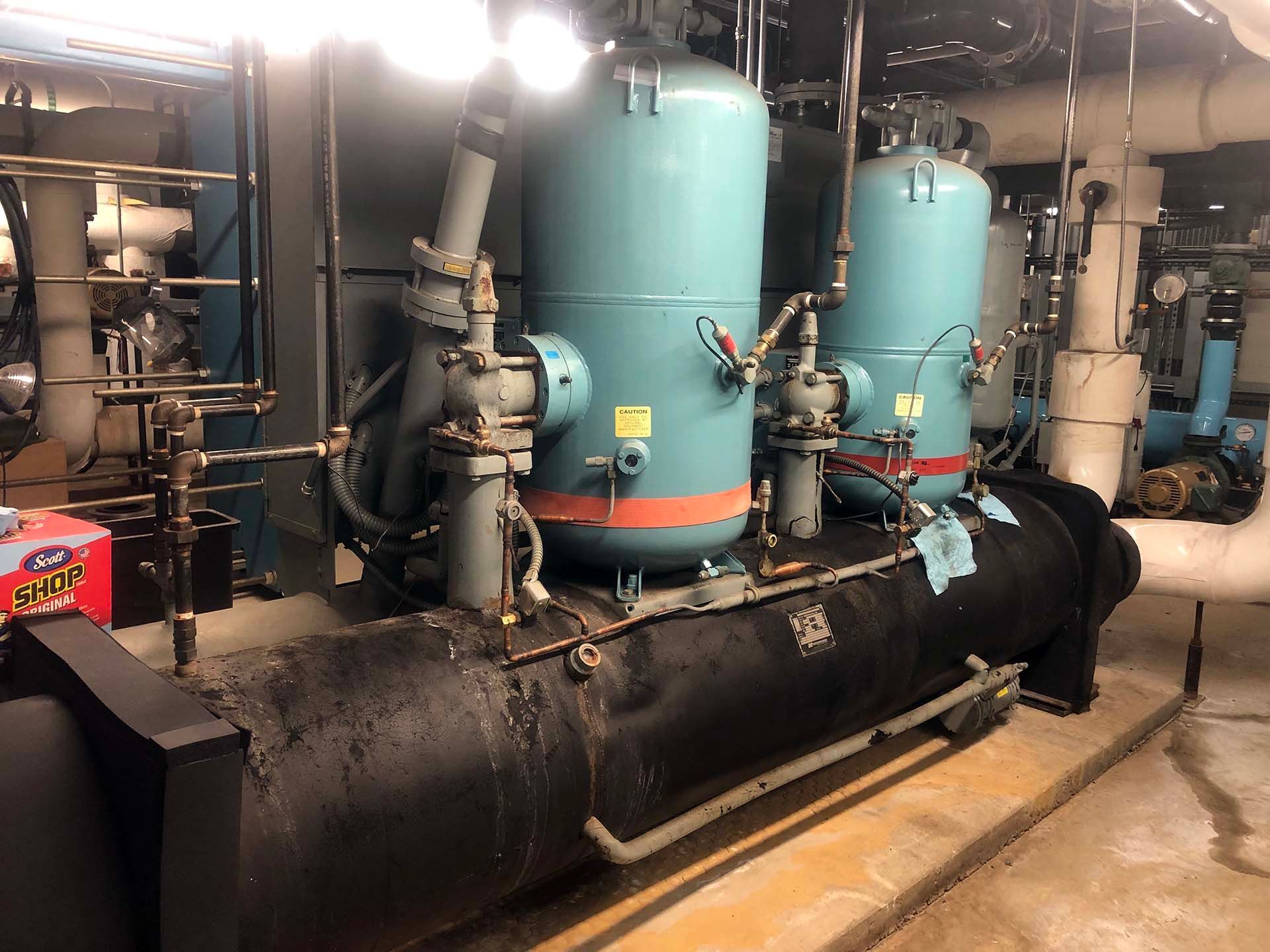 Industrial chiller with two blue tanks and black pipe in a machinery room.