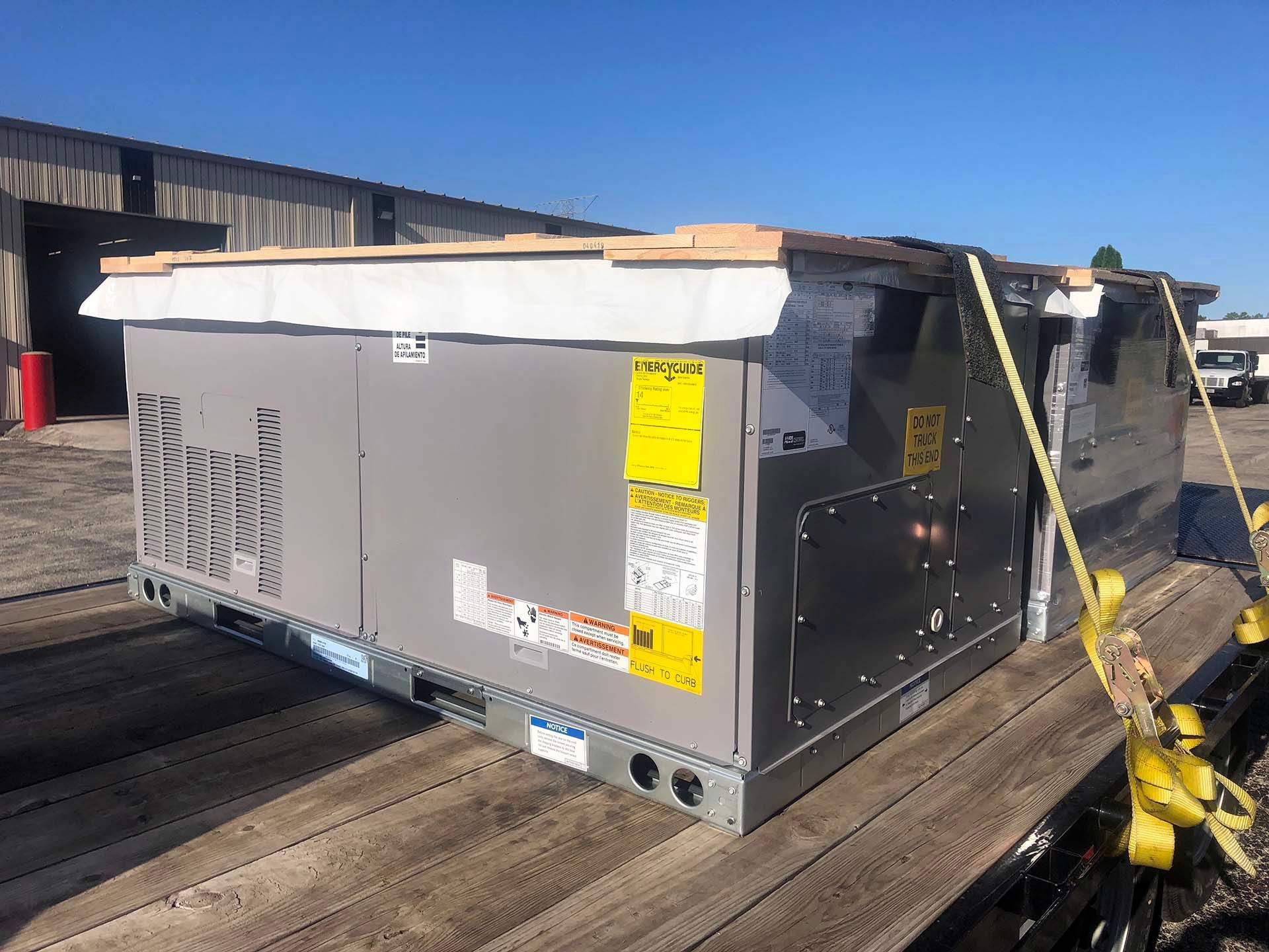 Large gray HVAC unit secured to a flatbed truck for transport, with a blue sky background.