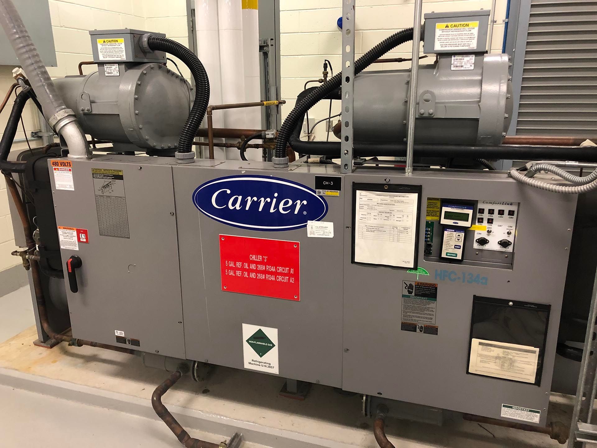 A gray Carrier chiller unit with motors, control panel, and pipes in an industrial setting.