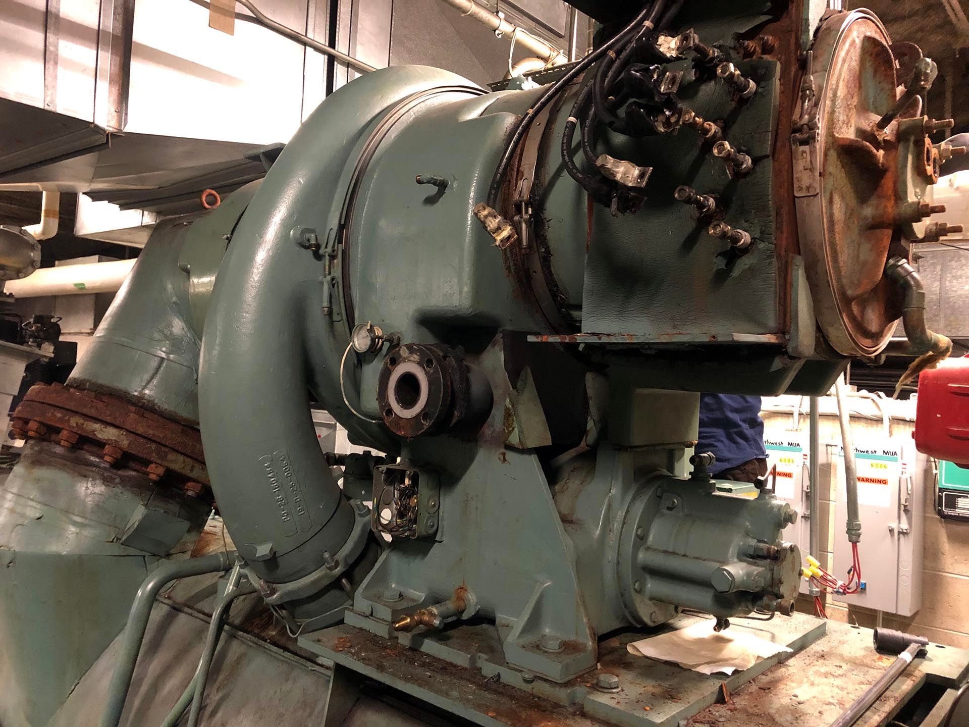 Large, teal industrial machine with pipes and attached components, indoors.