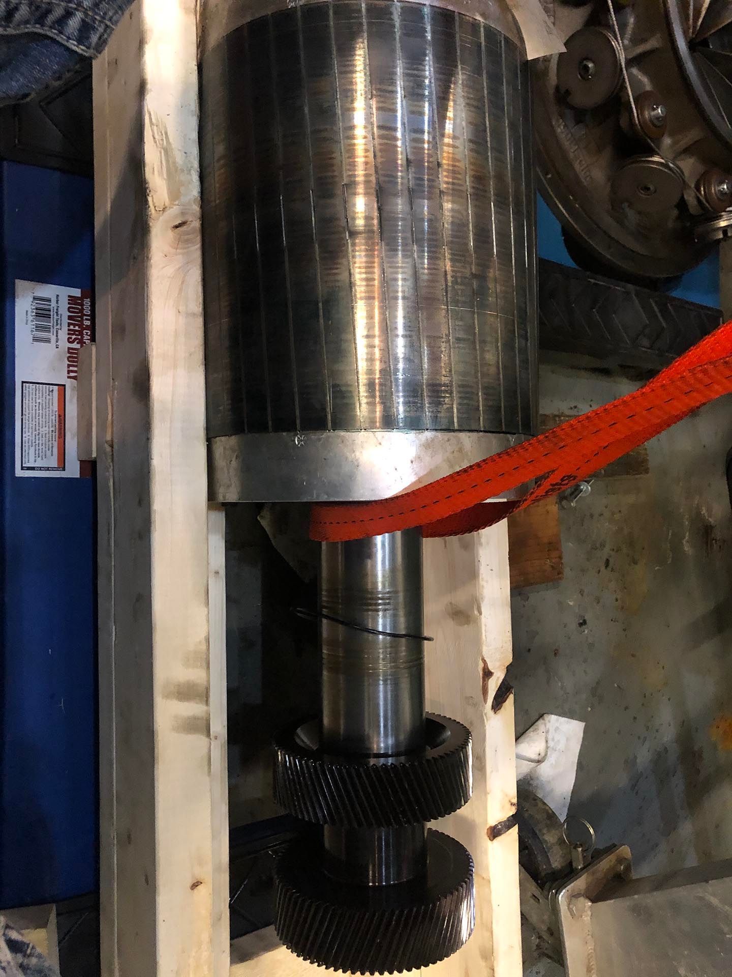 Large metal machine component, red strap around the motor, gears visible at the bottom.