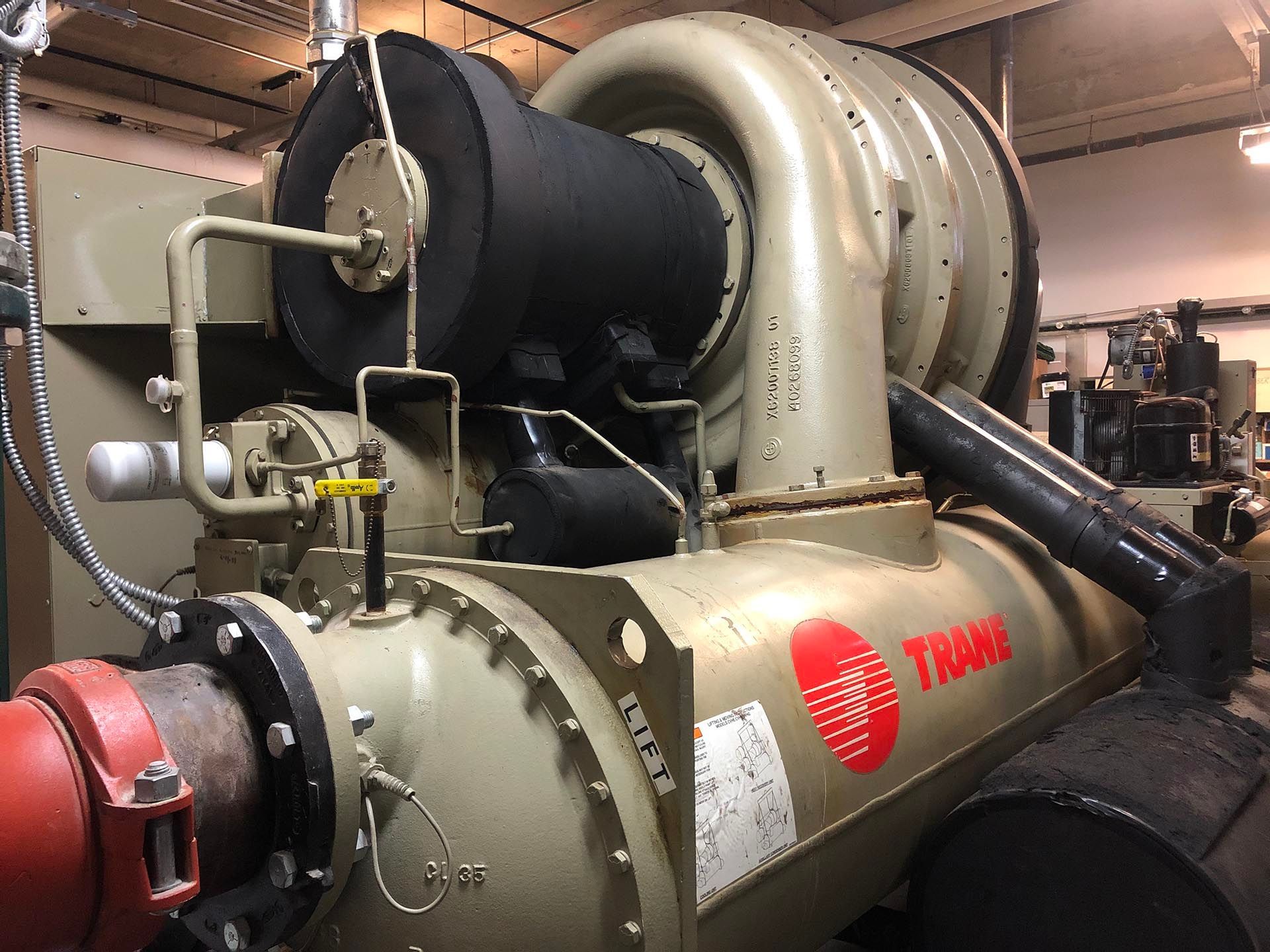 Large, industrial Trane chiller unit in a mechanical room, featuring pipes and insulation.