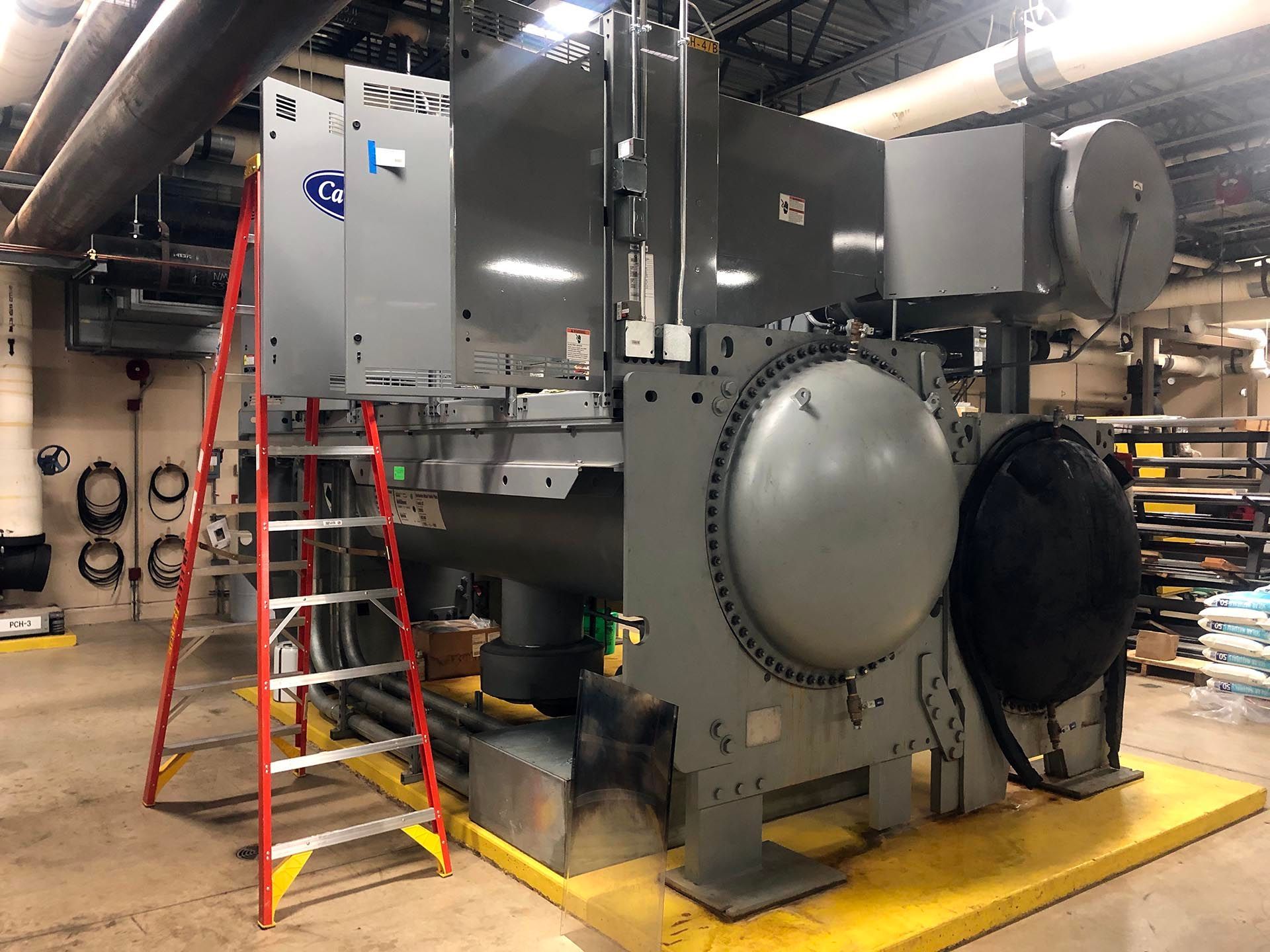 Large industrial chiller unit with gray exterior; red ladder alongside.