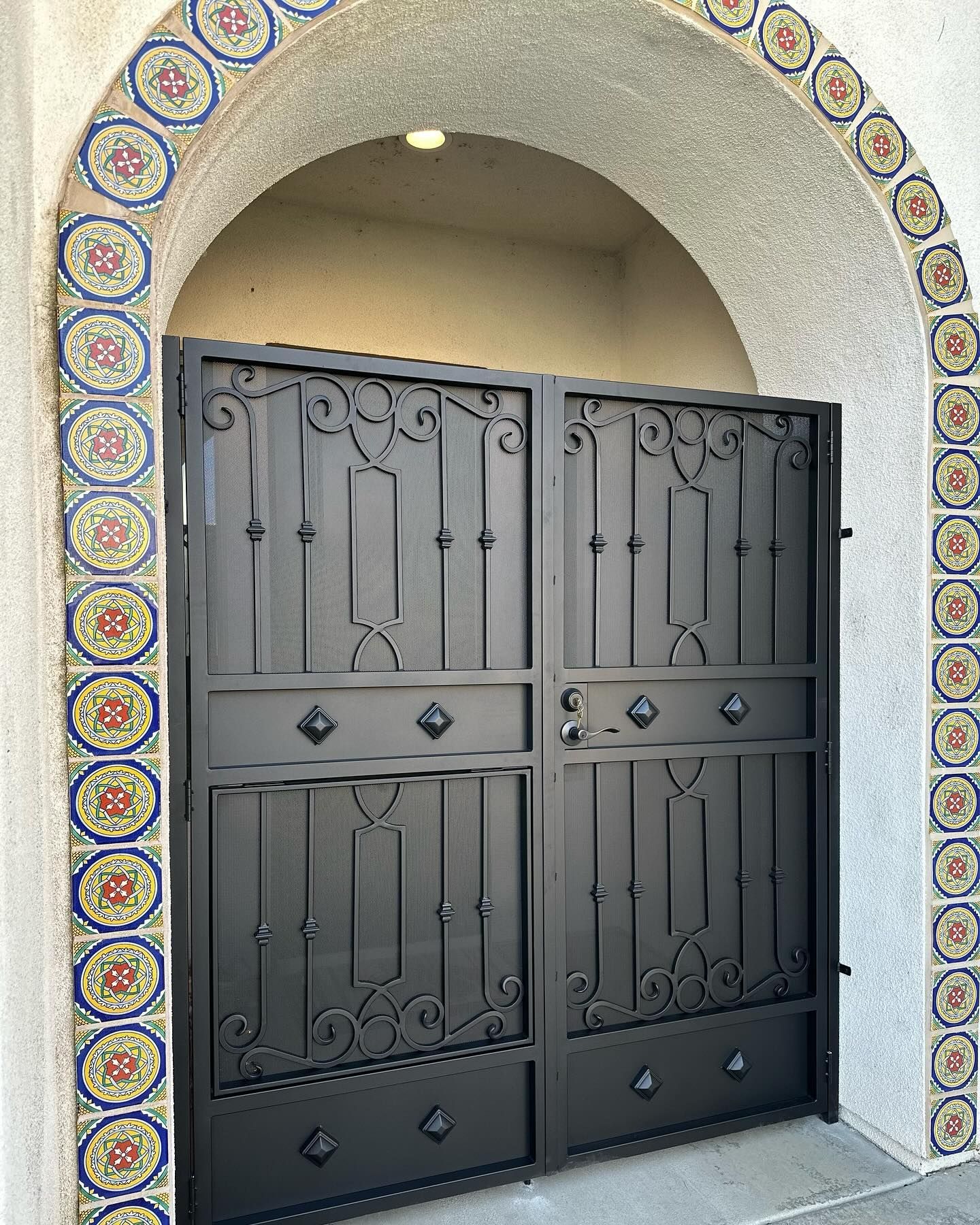 A black wrought iron gate with a tiled arch around it.