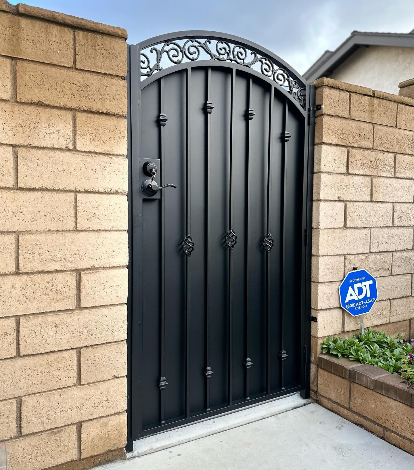 A black gate is sitting in front of a brick wall.