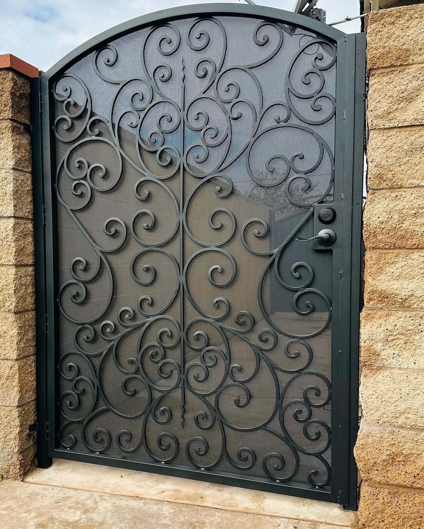 A wrought iron gate with swirls on it is next to a brick wall.