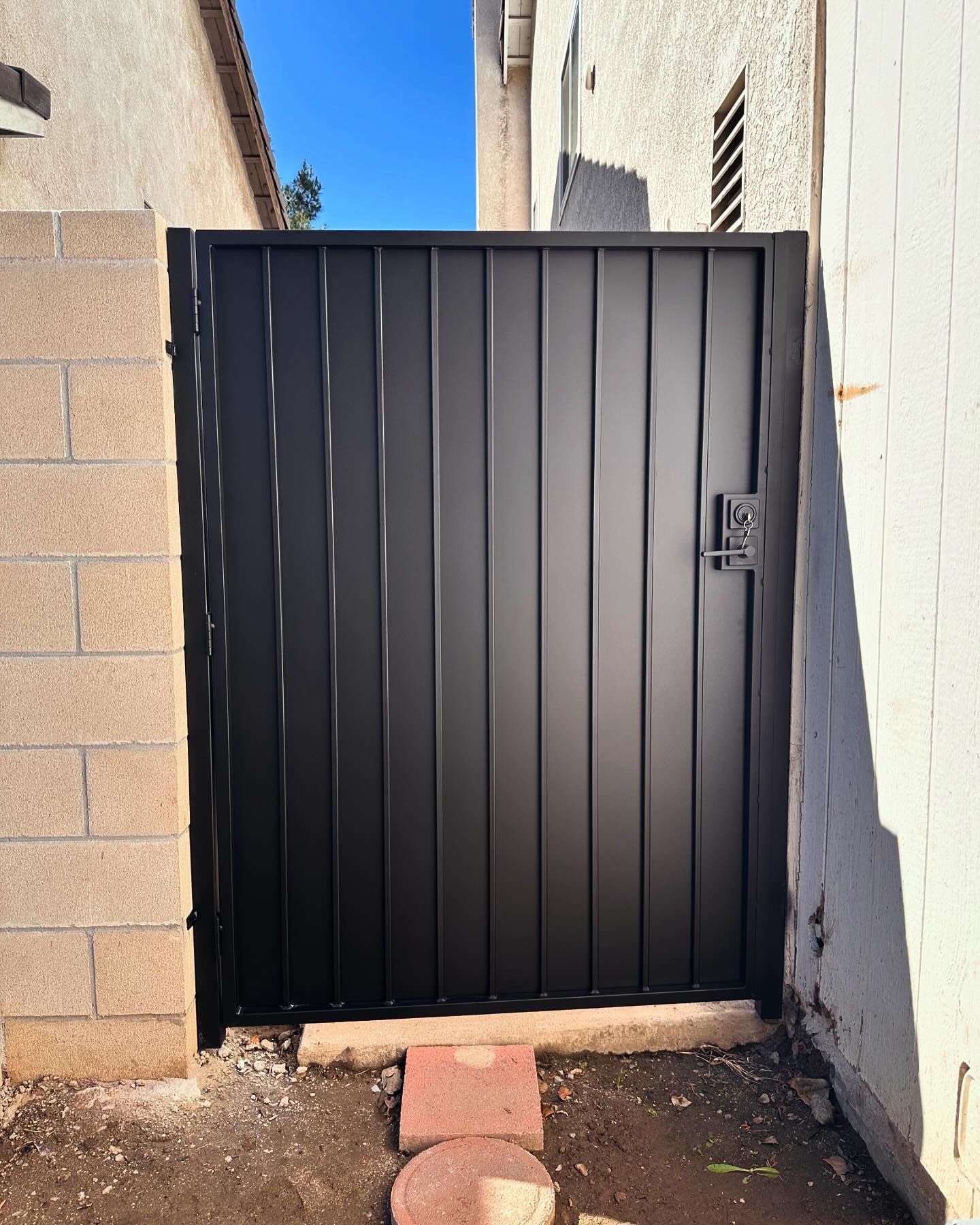 A black gate is sitting next to a brick wall