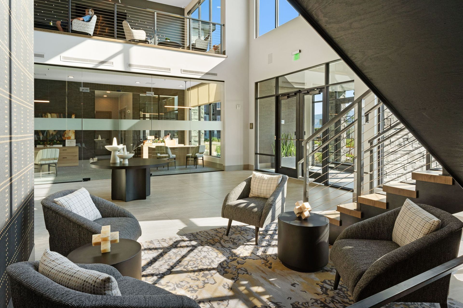 Lobby with seating area, stairs, glass walls, and a view of a second-floor balcony. Natural light floods the space.