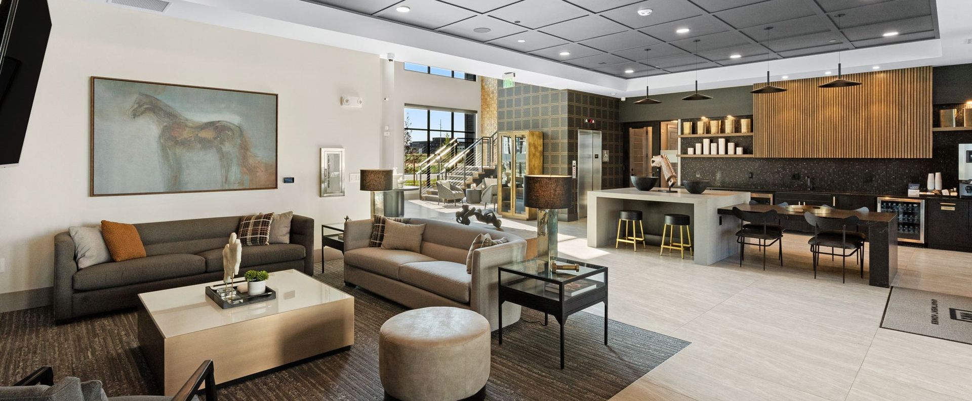 Upscale living room with a horse painting, seating area, and kitchen. Neutral colors, natural light.