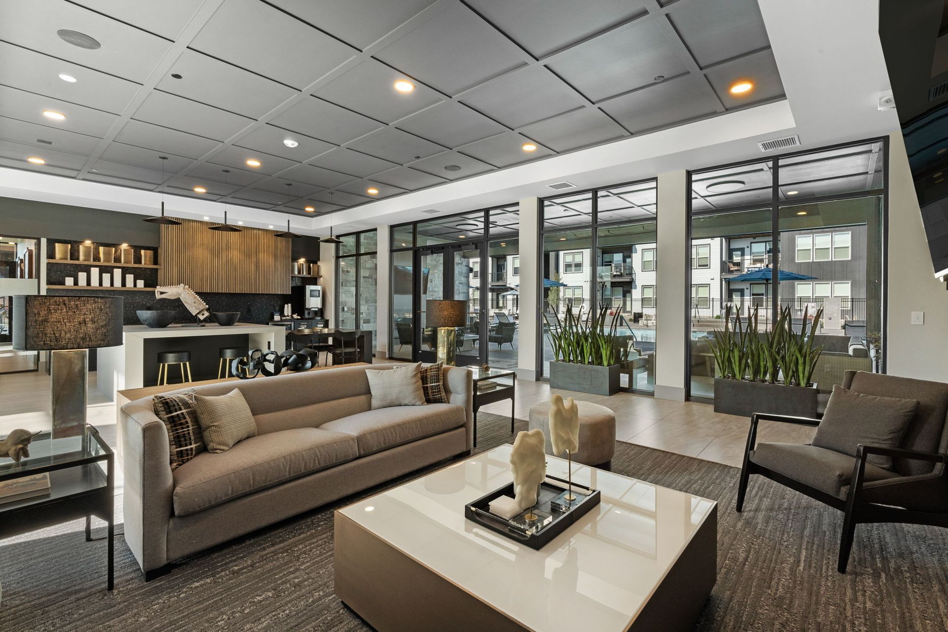 Modern lounge area with gray sofa, armchairs, and glass doors overlooking an outdoor space.