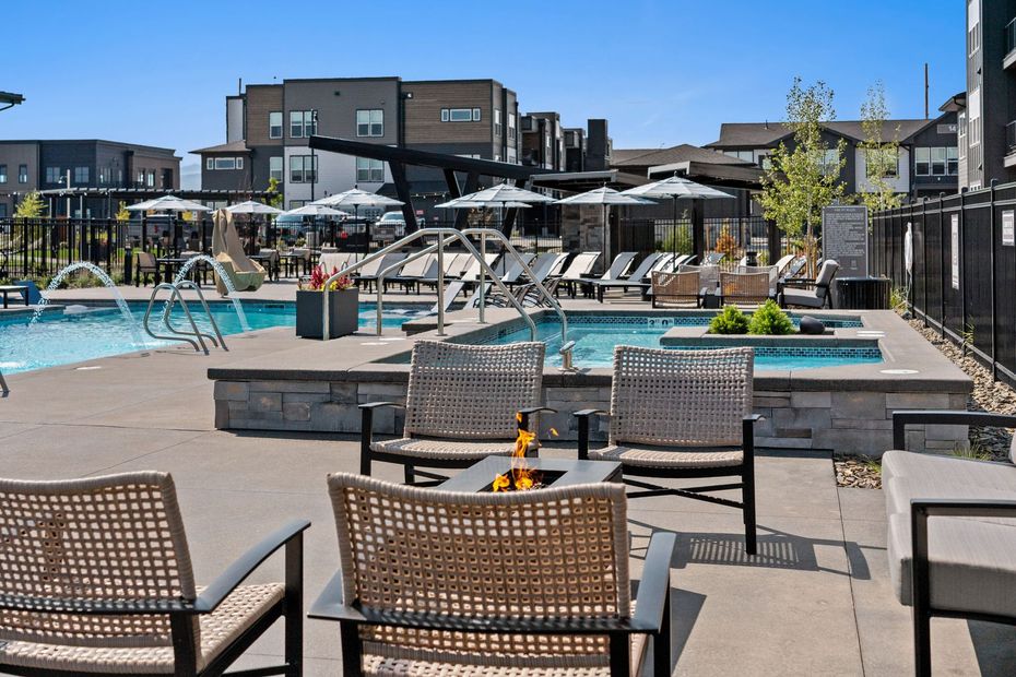 Pool area with lounge chairs, a fire pit, and a jacuzzi. Modern buildings in the background.