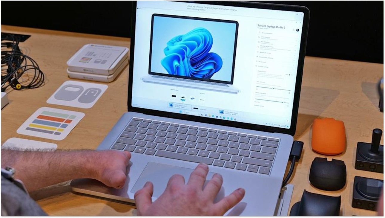 A pair of hands, one without fingers, using a touchpad on a Surface Laptop Studio 2.