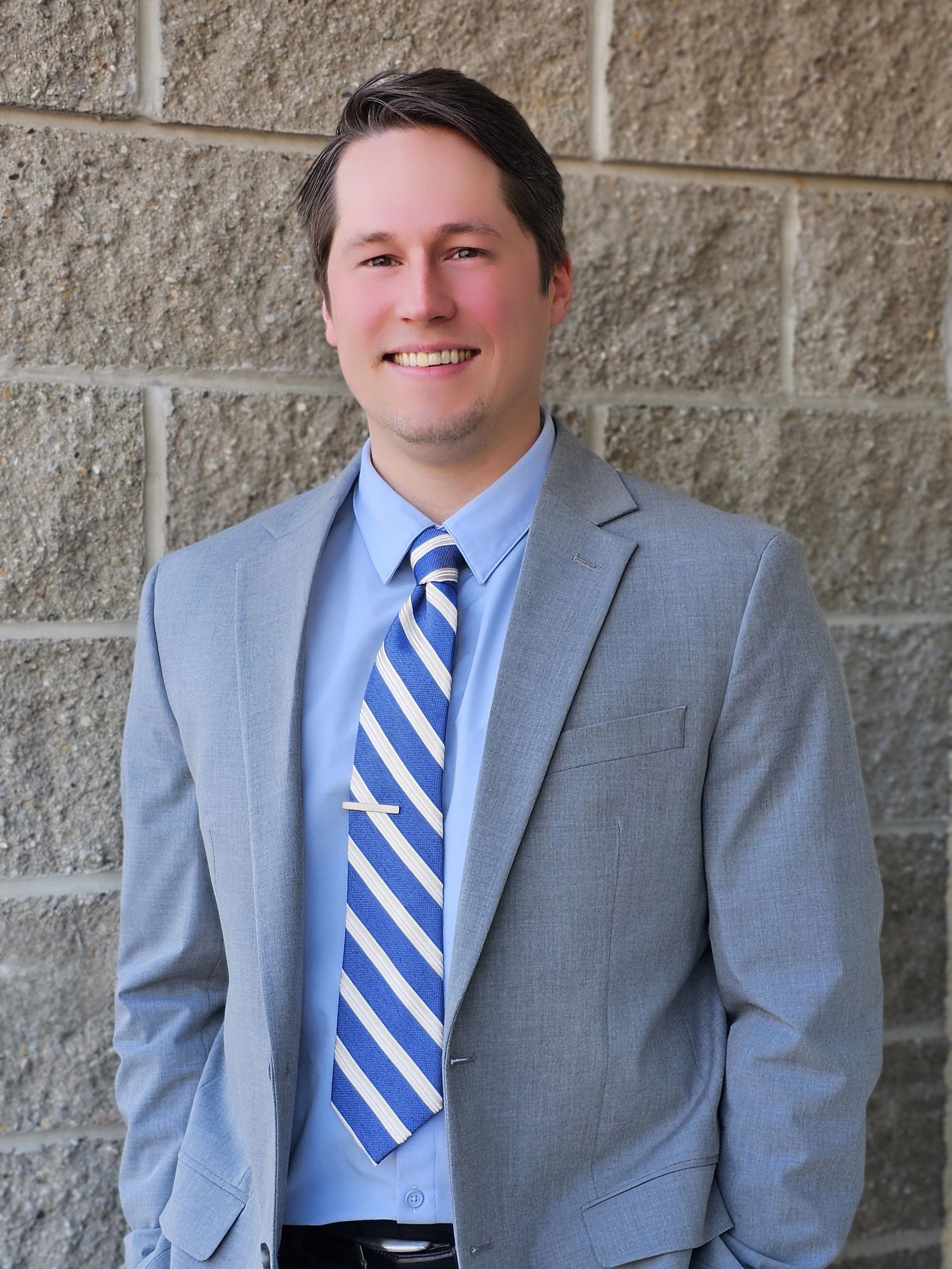 A man in a suit and tie is standing in front of a brick wall