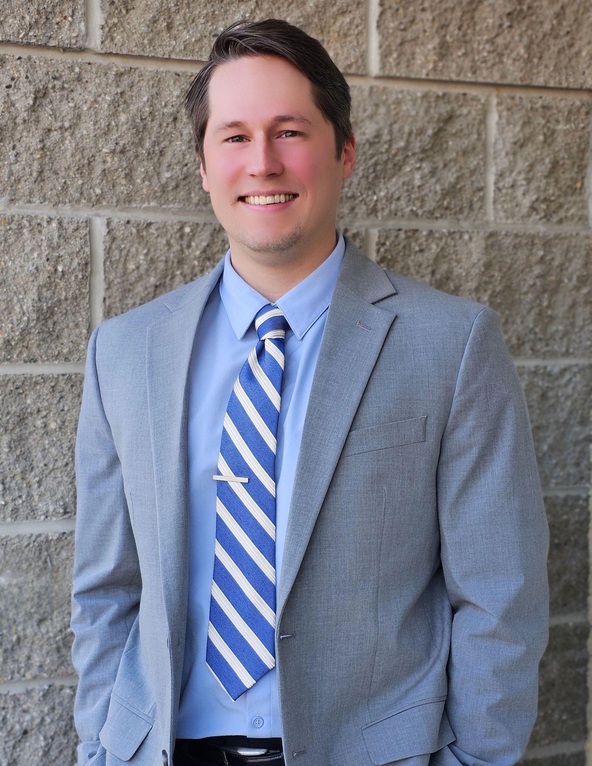 A man in a suit and tie is standing in front of a brick wall