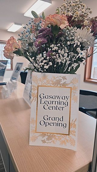 A vase of flowers is sitting on a table next to a sign that says `` grand opening ''.