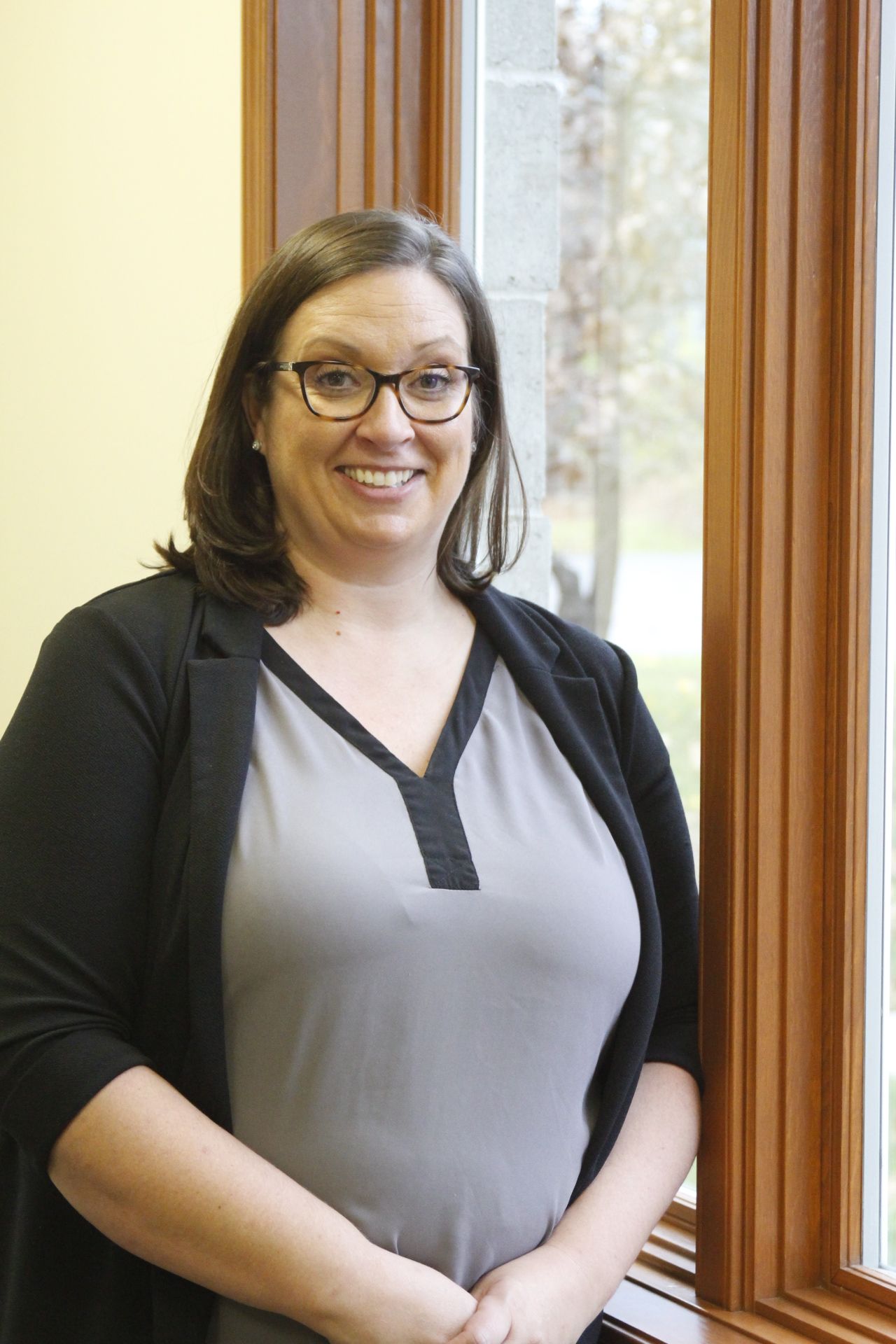 A woman wearing glasses is standing in front of a window.