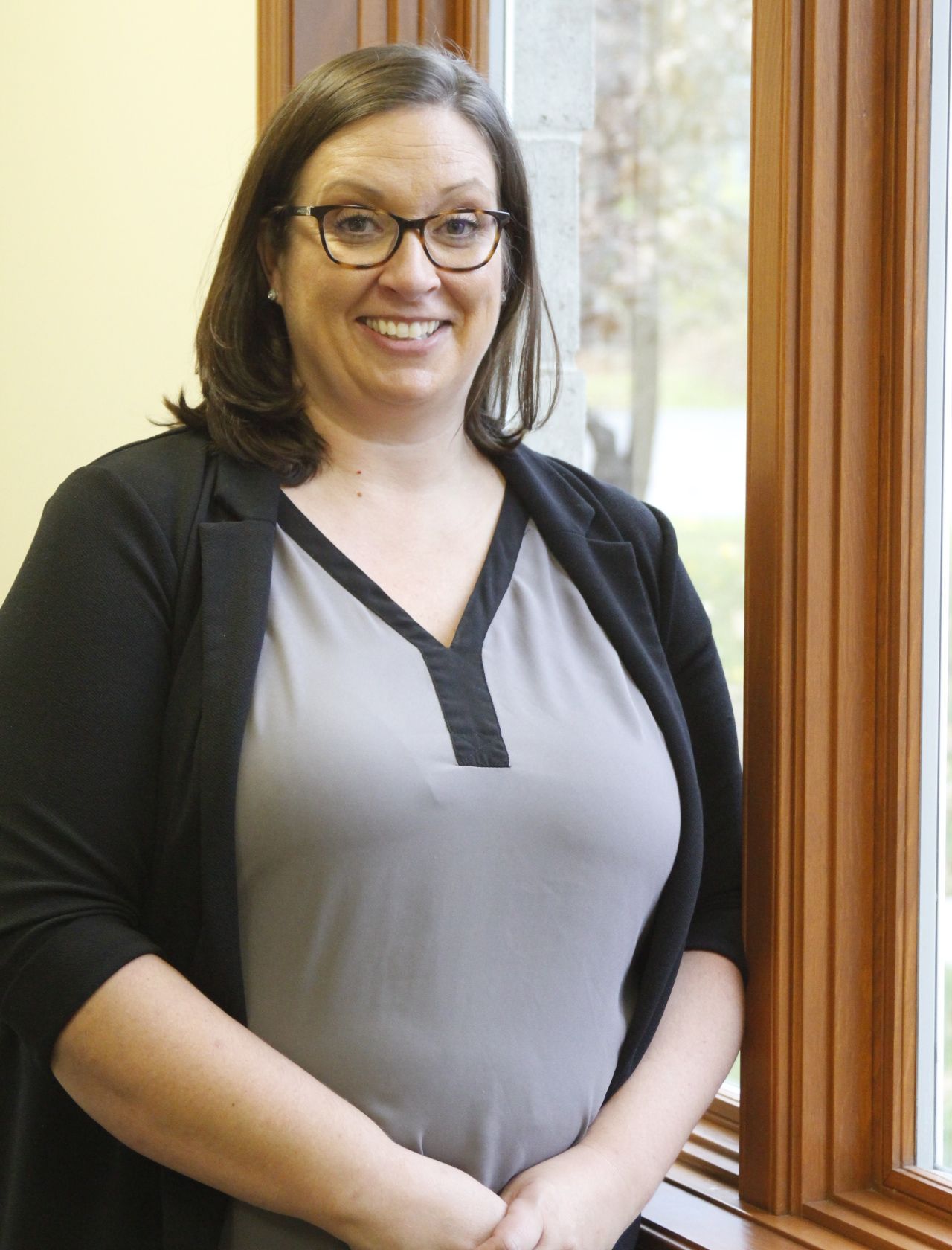 A woman wearing glasses is standing in front of a window