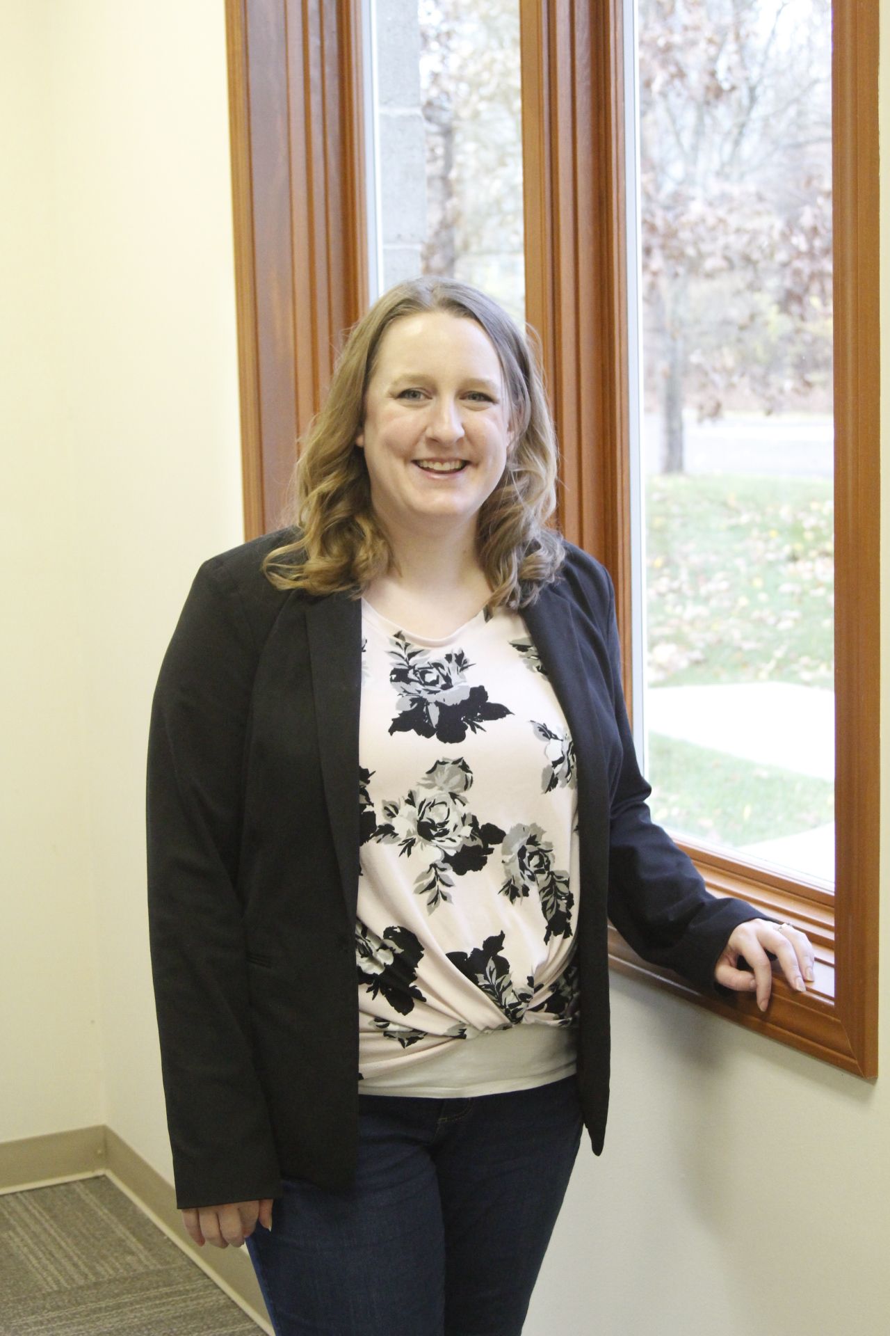 A woman is standing in front of a window and smiling.