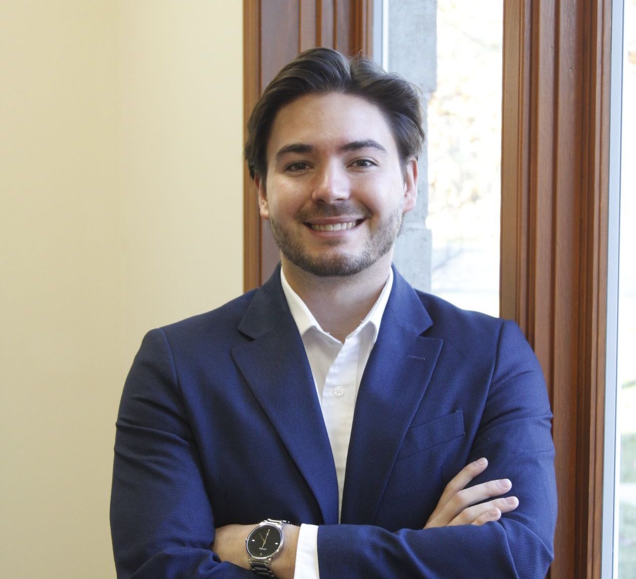 A man in a blue suit is smiling with his arms crossed