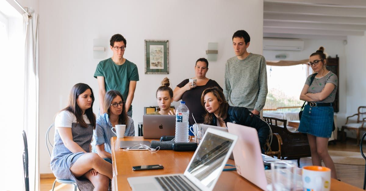 A group of people are sitting around a table with laptops.
